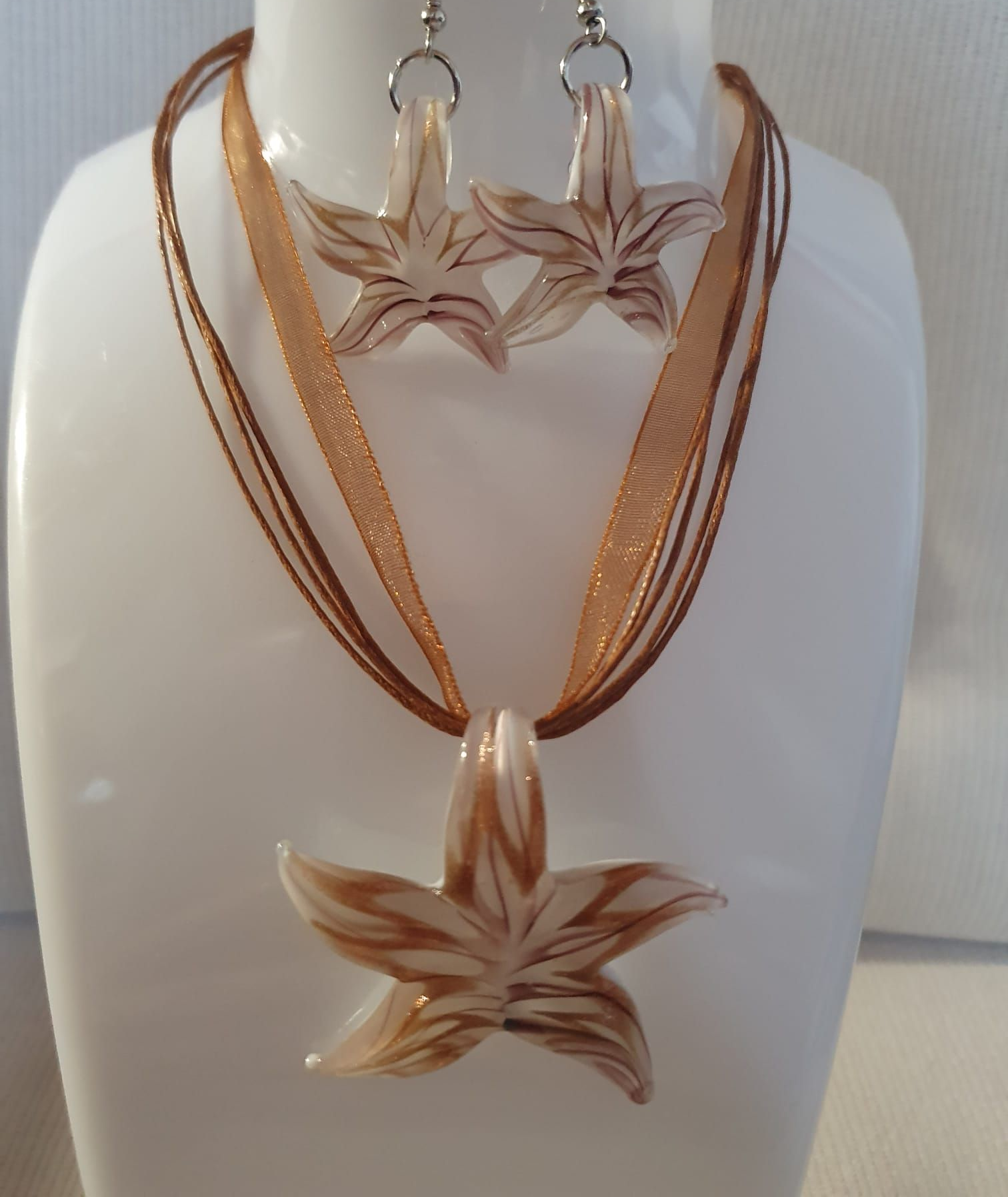 Buste blanc orné d'un collier à fleurs étoilées couleur cuivre et de boucles d'oreilles assorties, exposé