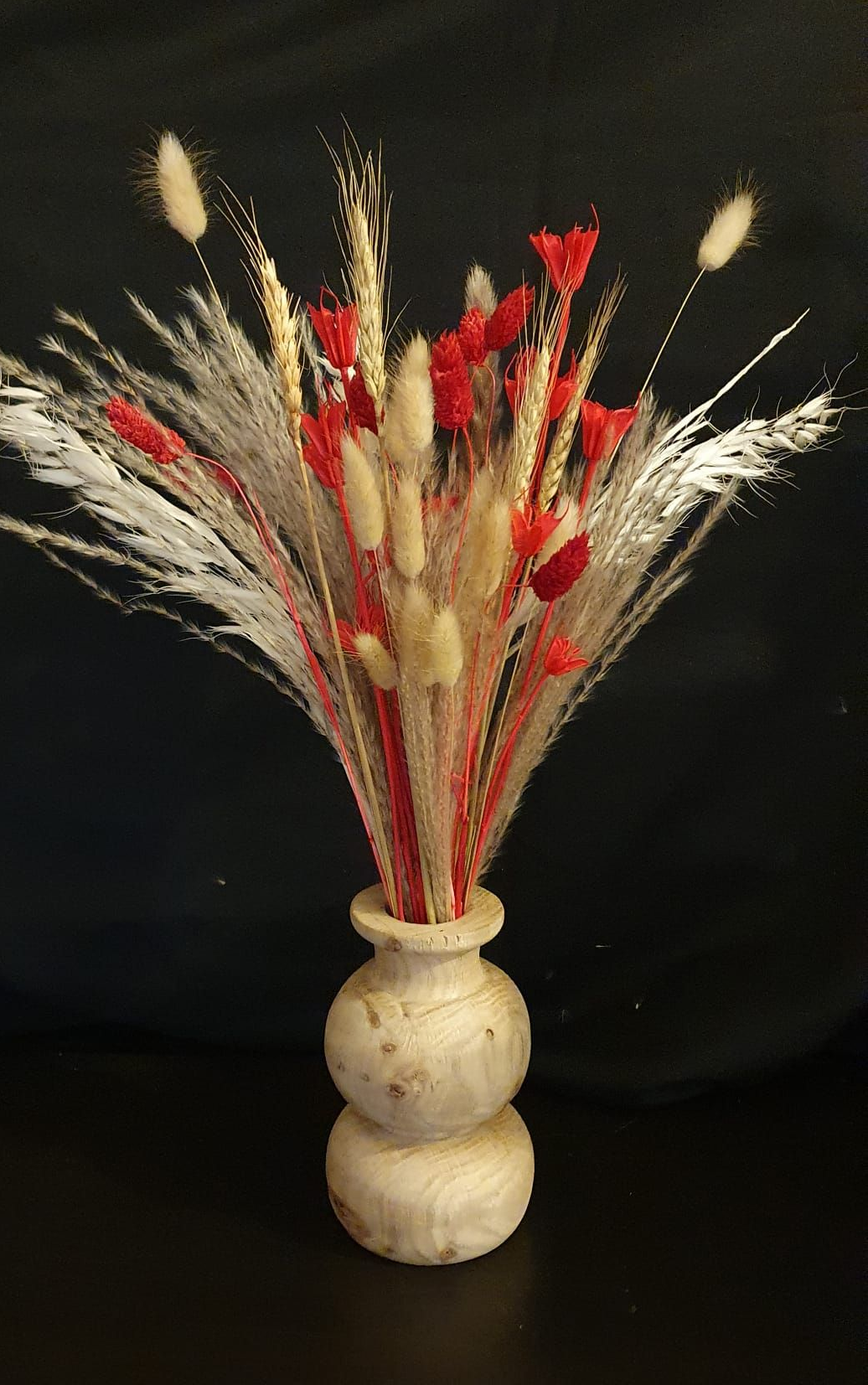 Un petit vase blanc contenant des herbes séchées rouges, beiges et blanches sur fond noir
