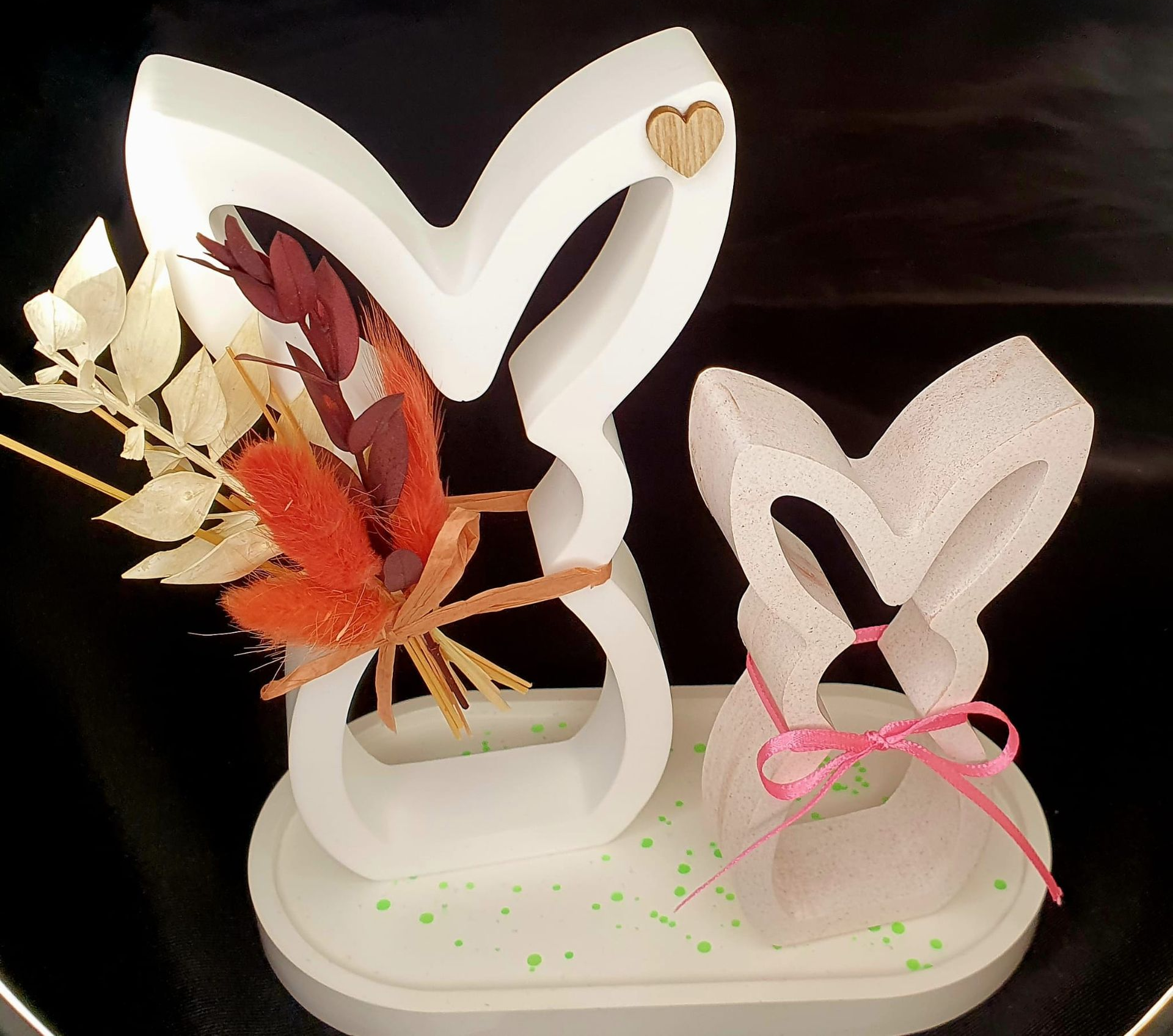 Décoration de lapin en papier blanc avec des feuilles orange et un lapin portant un nœud rose sur un plateau, sur fond sombre