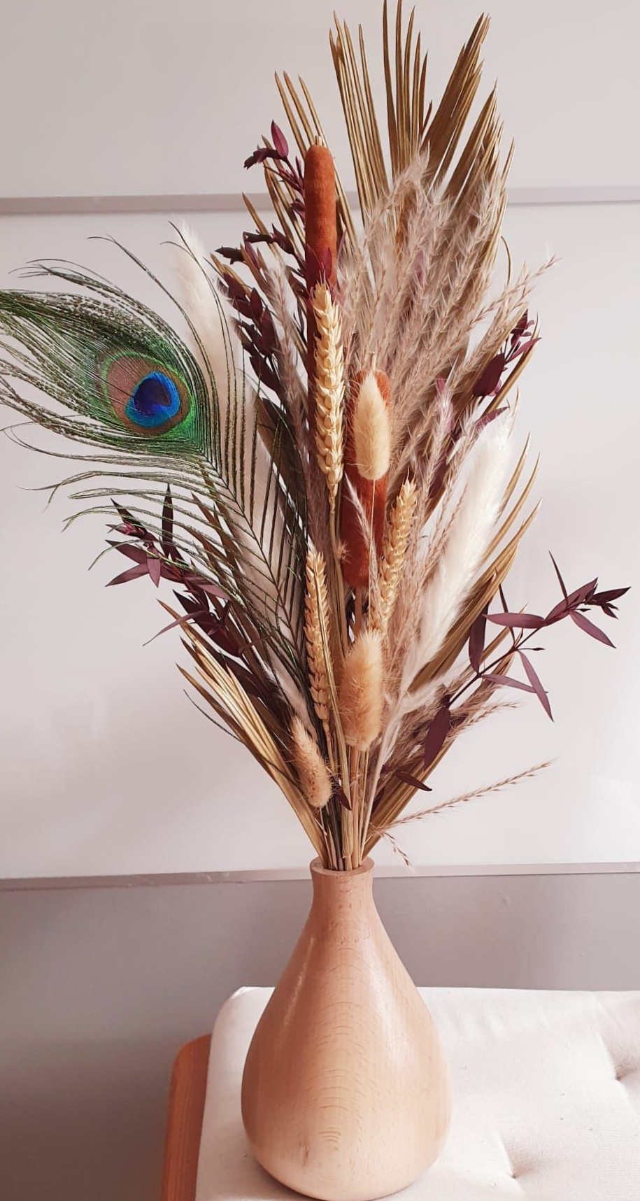 Grand arrangement floral séché avec une plume de paon dans un vase beige sur une surface blanche