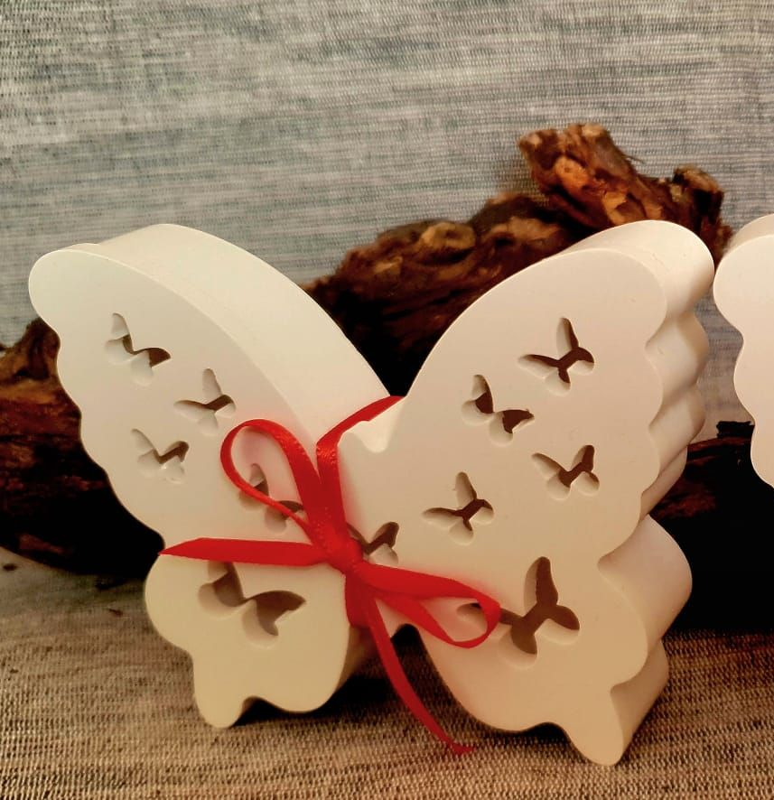 Décoration en bois en forme de papillon, nouée avec un ruban rouge, sur un fond rustique.