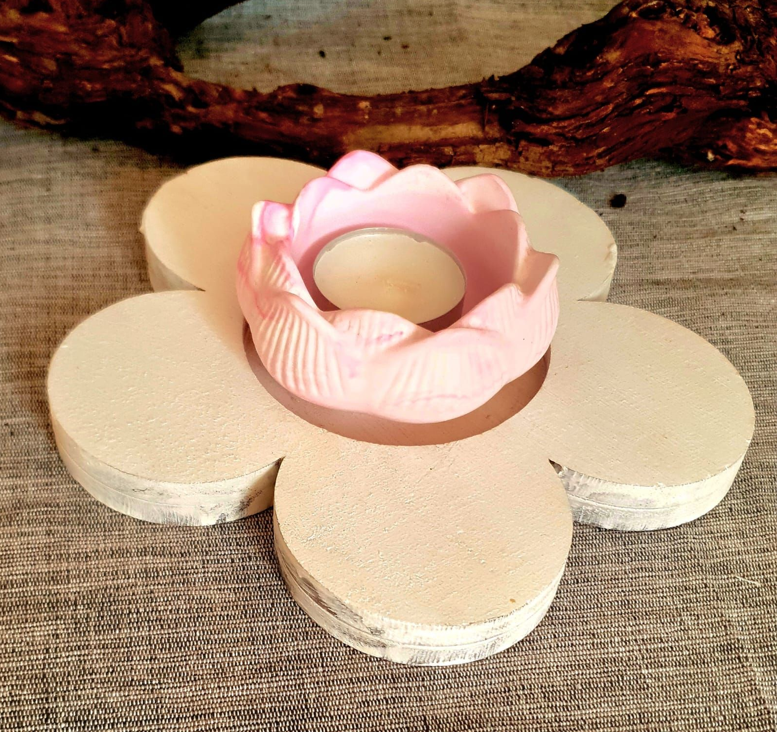 Un bougeoir en forme de fleur rose posé sur une surface en toile de jute, avec une branche en bois derrière.