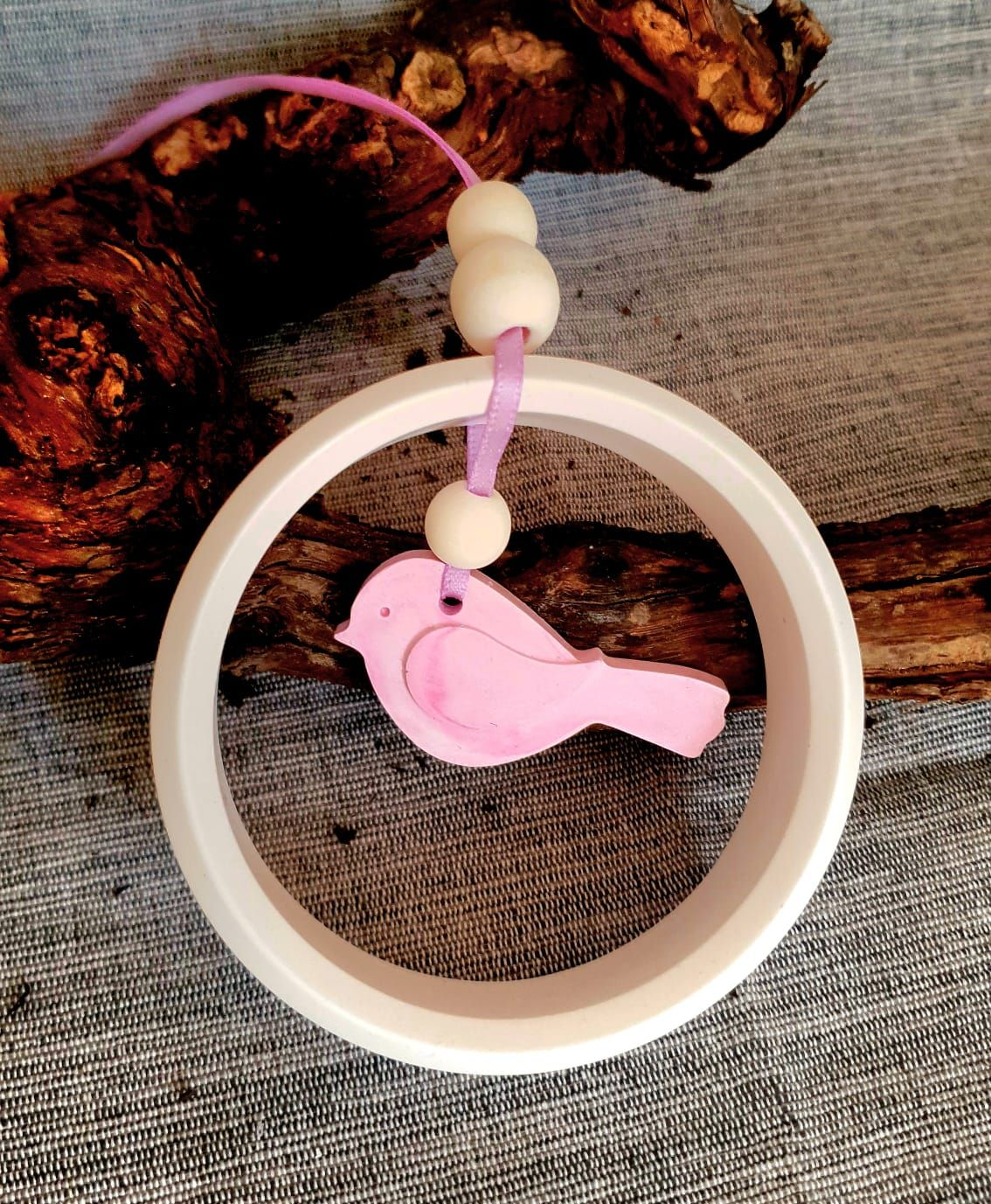 Breloque oiseau rose suspendue à l'intérieur d'un anneau blanc sur un fond de tissu texturé