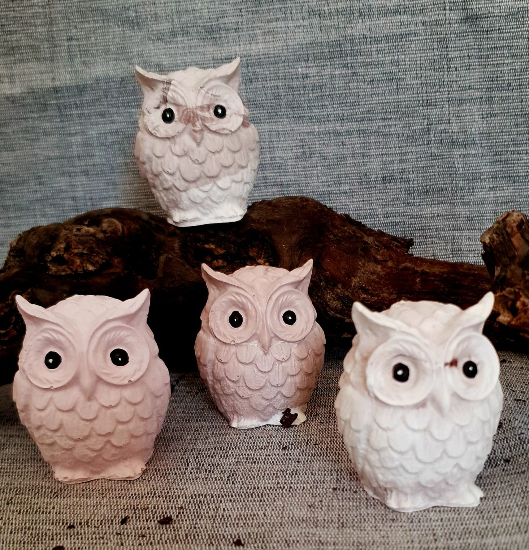 Cinq figurines décoratives de hiboux roses, blancs et bruns sur une surface grise texturée
