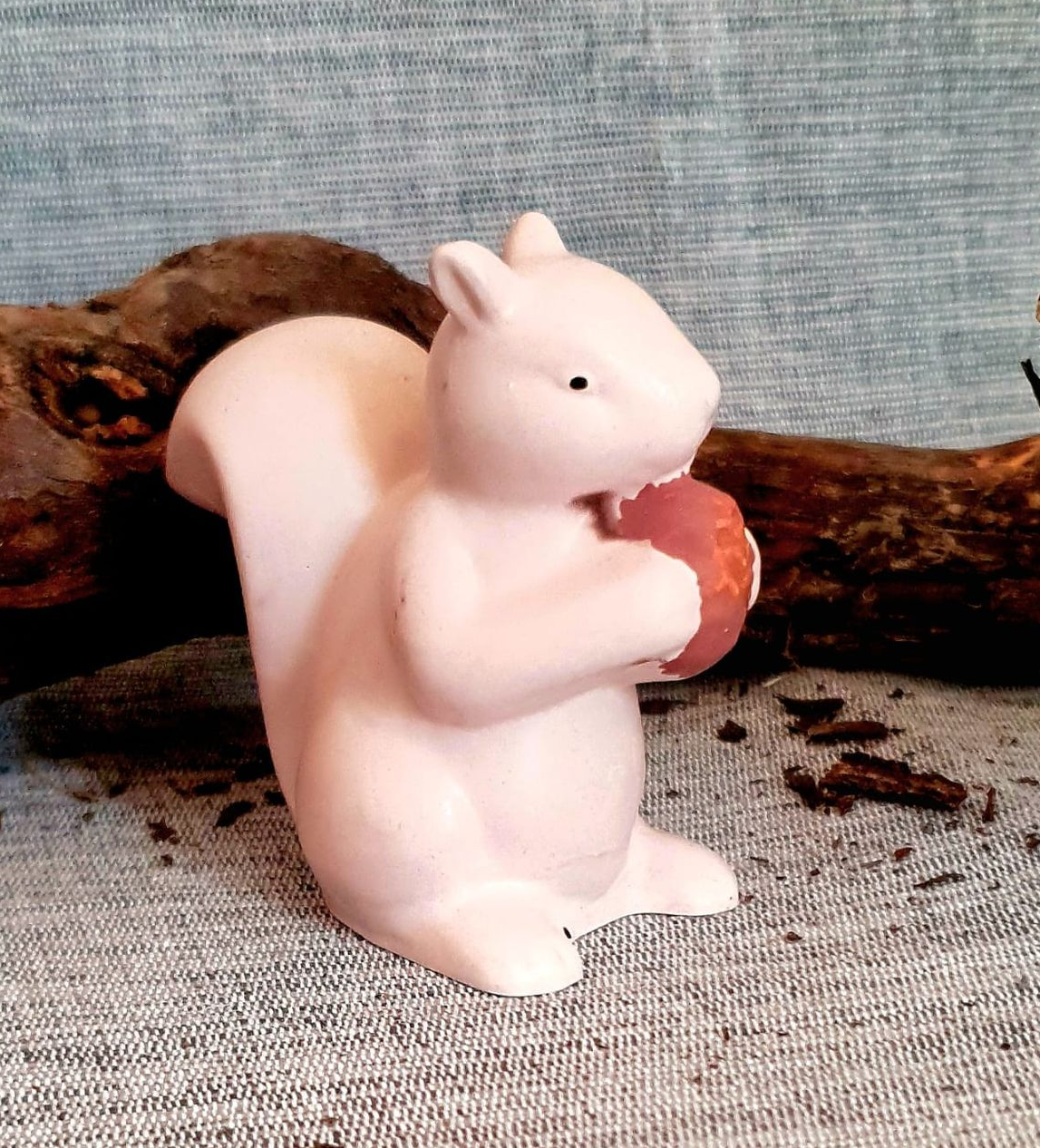 Figurine d'écureuil rose tenant un gland rouge sur fond de tissu gris