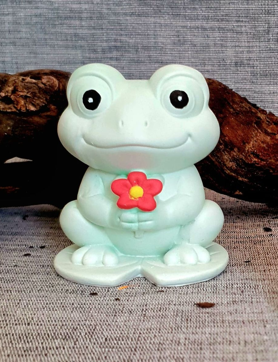 Figurine de grenouille vert menthe avec une fleur rose posée sur une surface grise