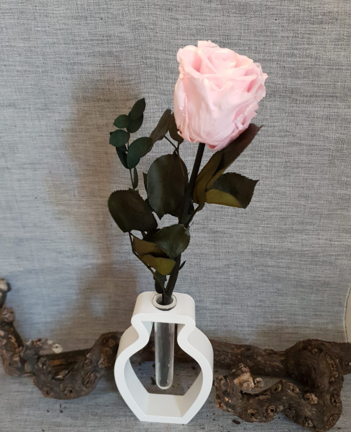 Rose rose dans un vase géométrique blanc sur une surface grise avec des accents de bois flotté