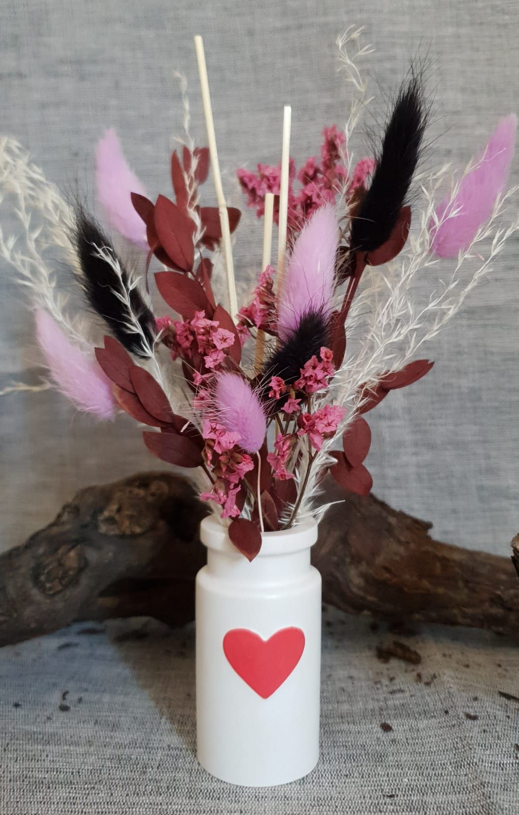 Vase en pot blanc orné d'un cœur rouge, contenant des fleurs séchées roses, rouges et noires.
