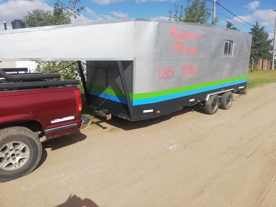Remolque de caravana gris estacionado junto a una camioneta roja en un camino de tierra