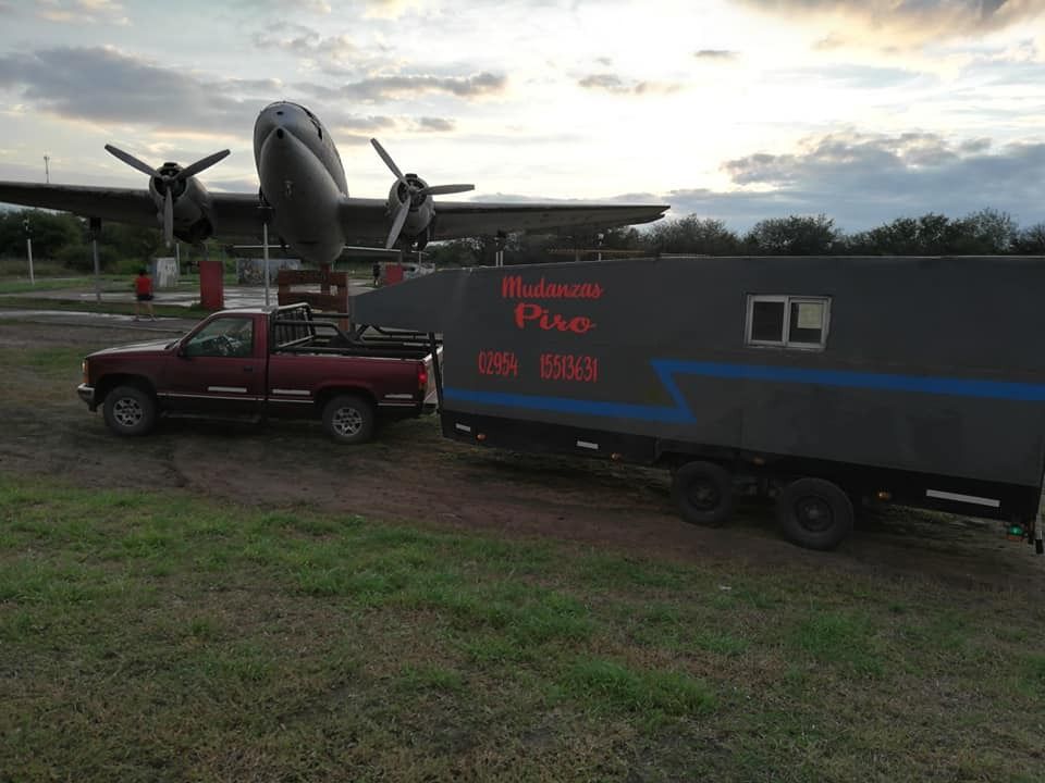 Camioneta roja remolcando un remolque negro con un avión estacionado detrás al atardecer.