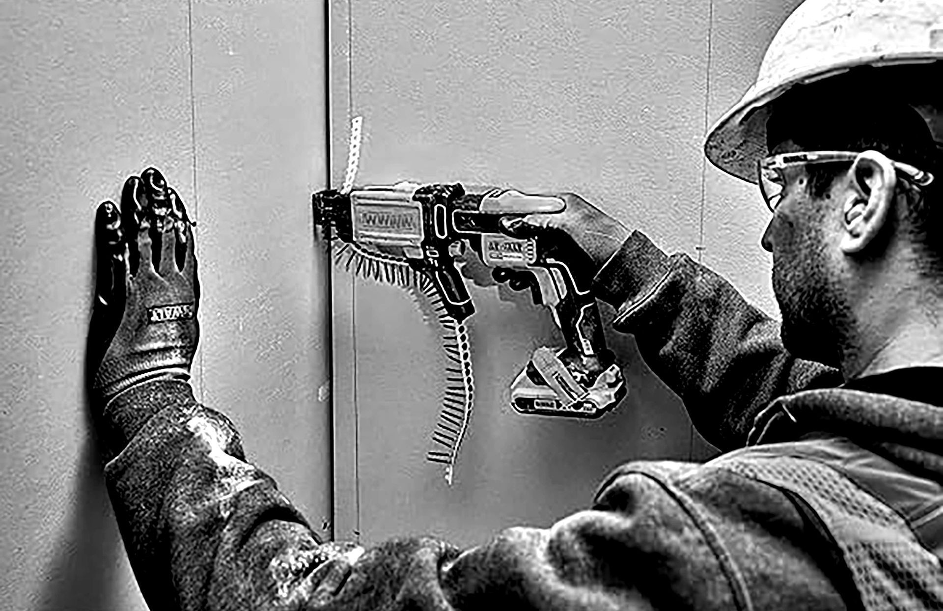 Worker in hard hat drilling into a wall with a power tool, using FRAMER'S FORCE screws.