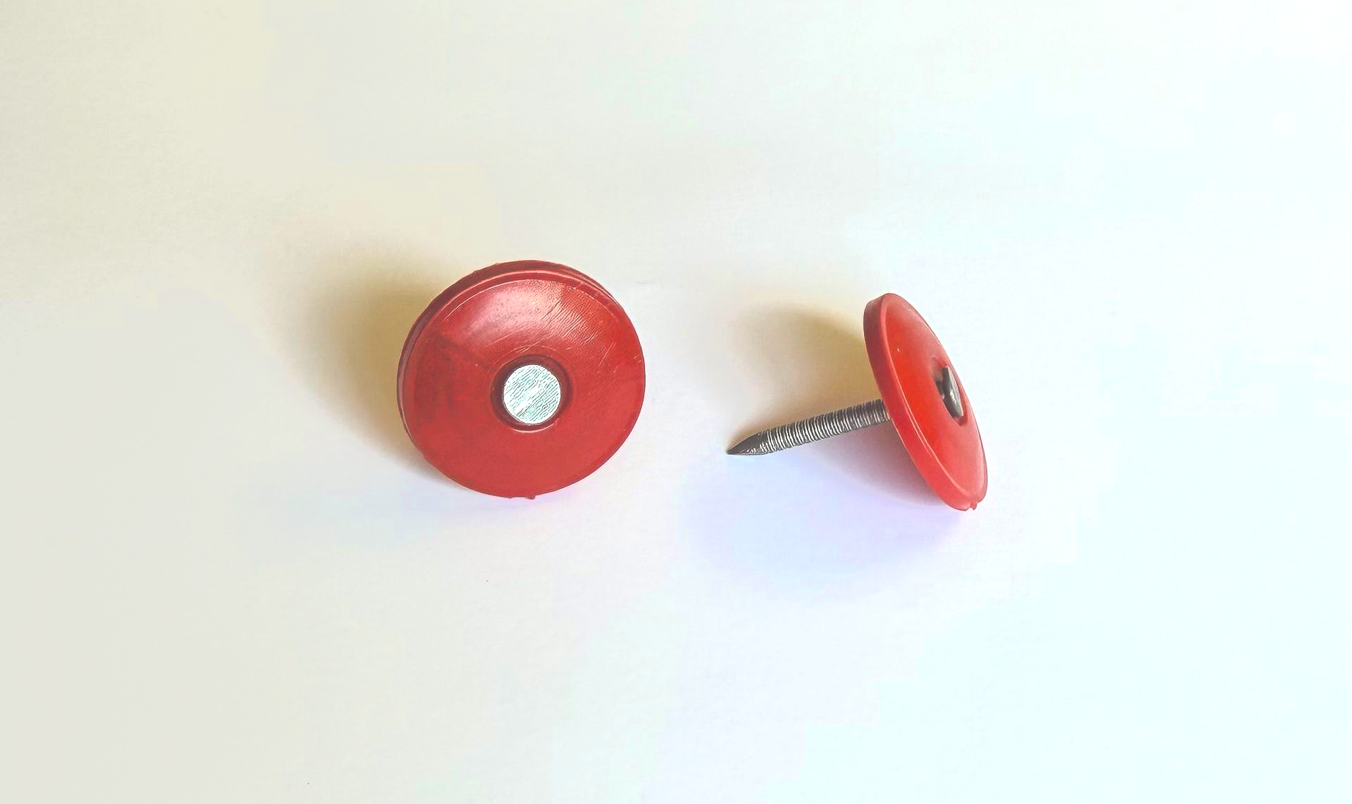 Two red thumbtacks on a white background, one lying flat and one tilted on its side