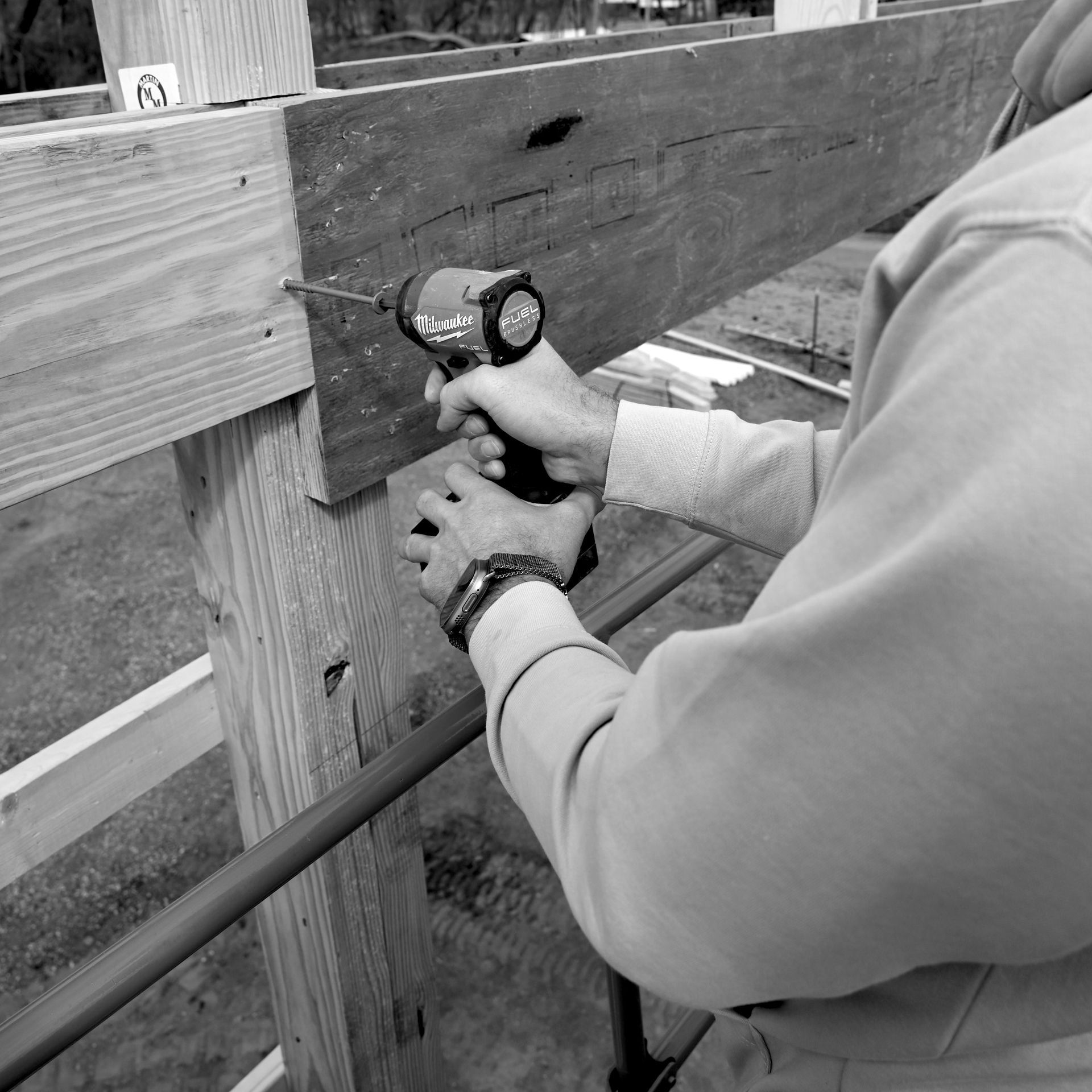 Person using a cordless drill to fasten a wooden board to a post outdoors.