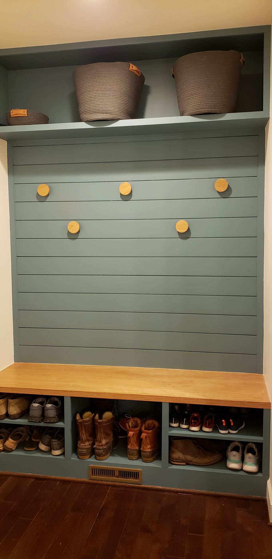 Empty retail display wall with mint-green slats, tan baskets on top, and cubbies with products below