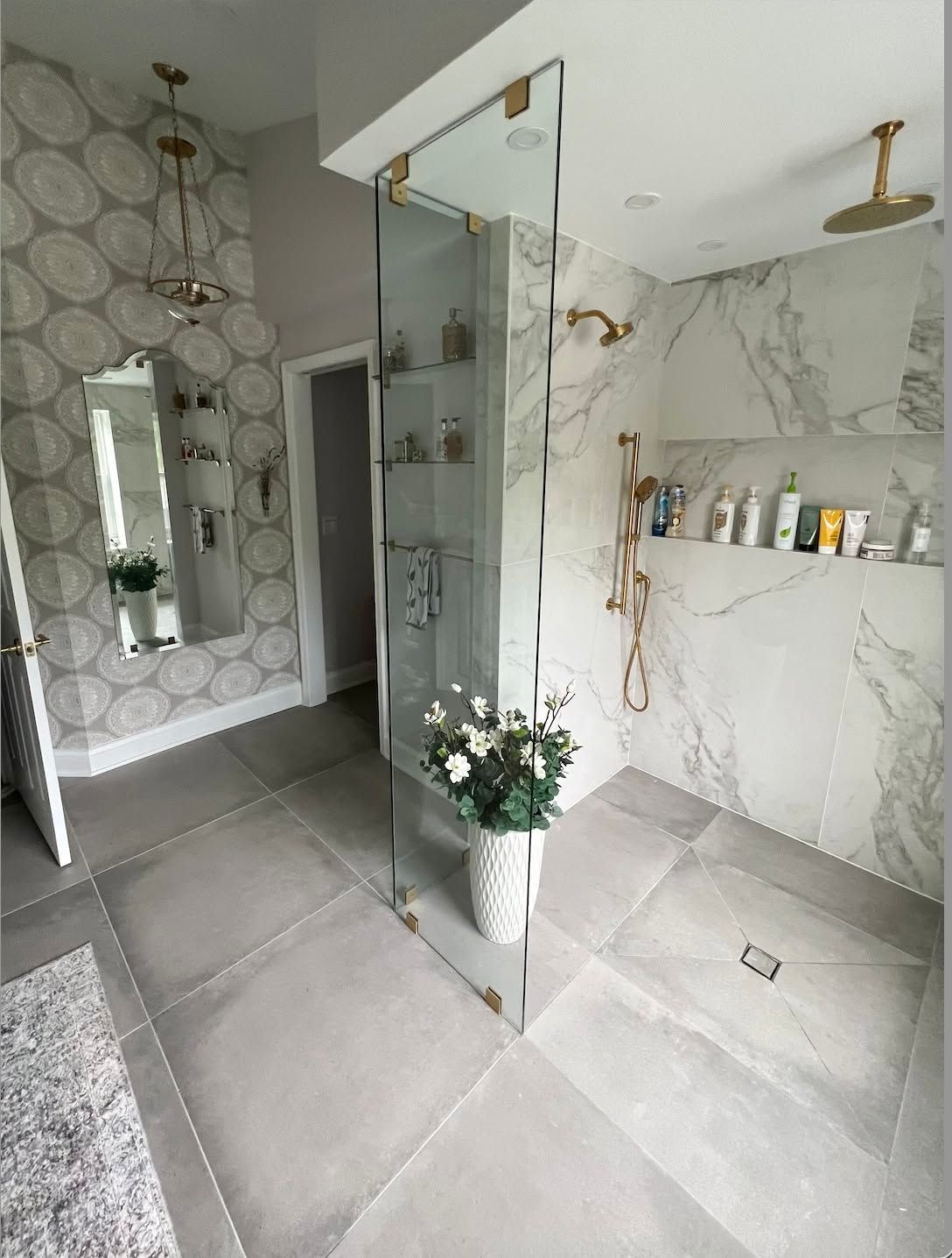Modern marble bathroom with glass shower, hex tile wall, and a vase of flowers