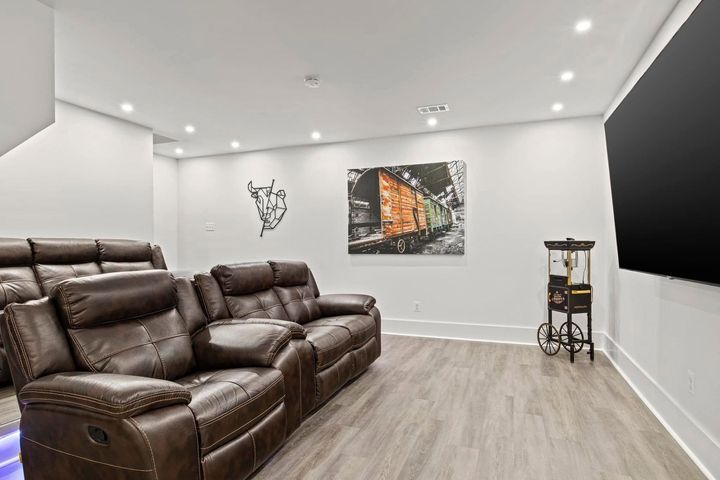 Modern living room with brown leather recliners, white walls, wood flooring, and abstract wall art