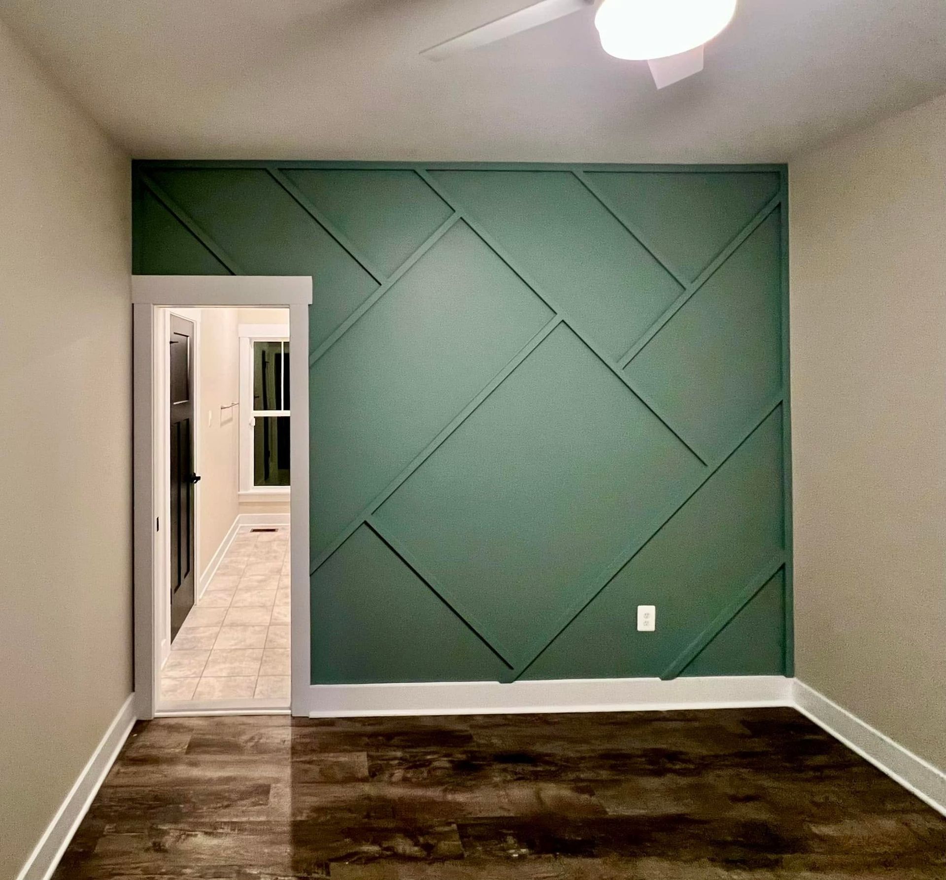 Empty room with green geometric accent wall and dark carpet, viewed through a doorway