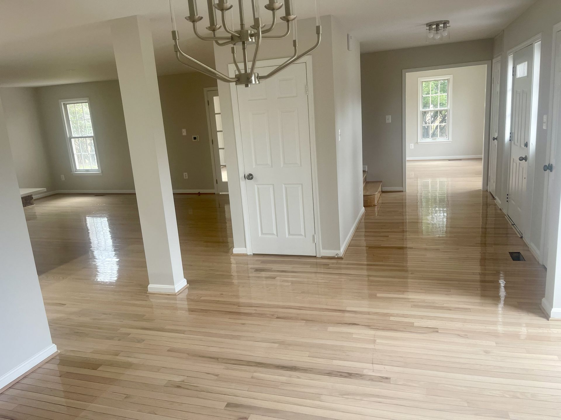 Empty bright room with polished hardwood floors, white walls, and a chandelier