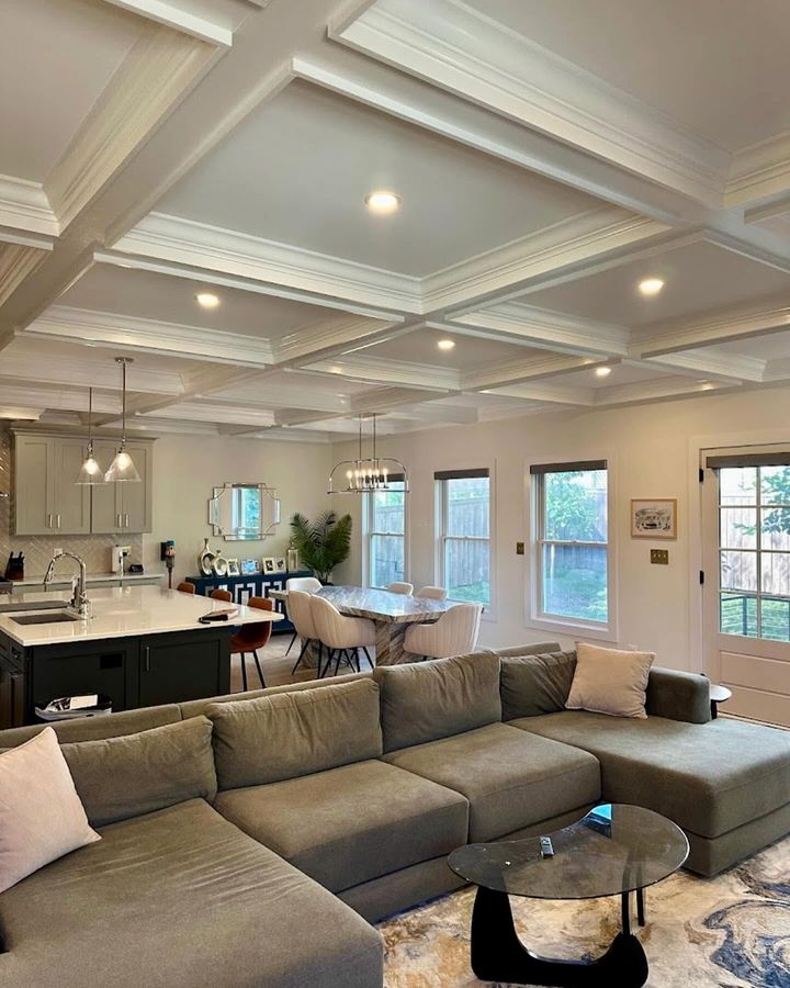 Bright living room with gray sectional, marble coffee table, coffered ceiling, and open kitchen area