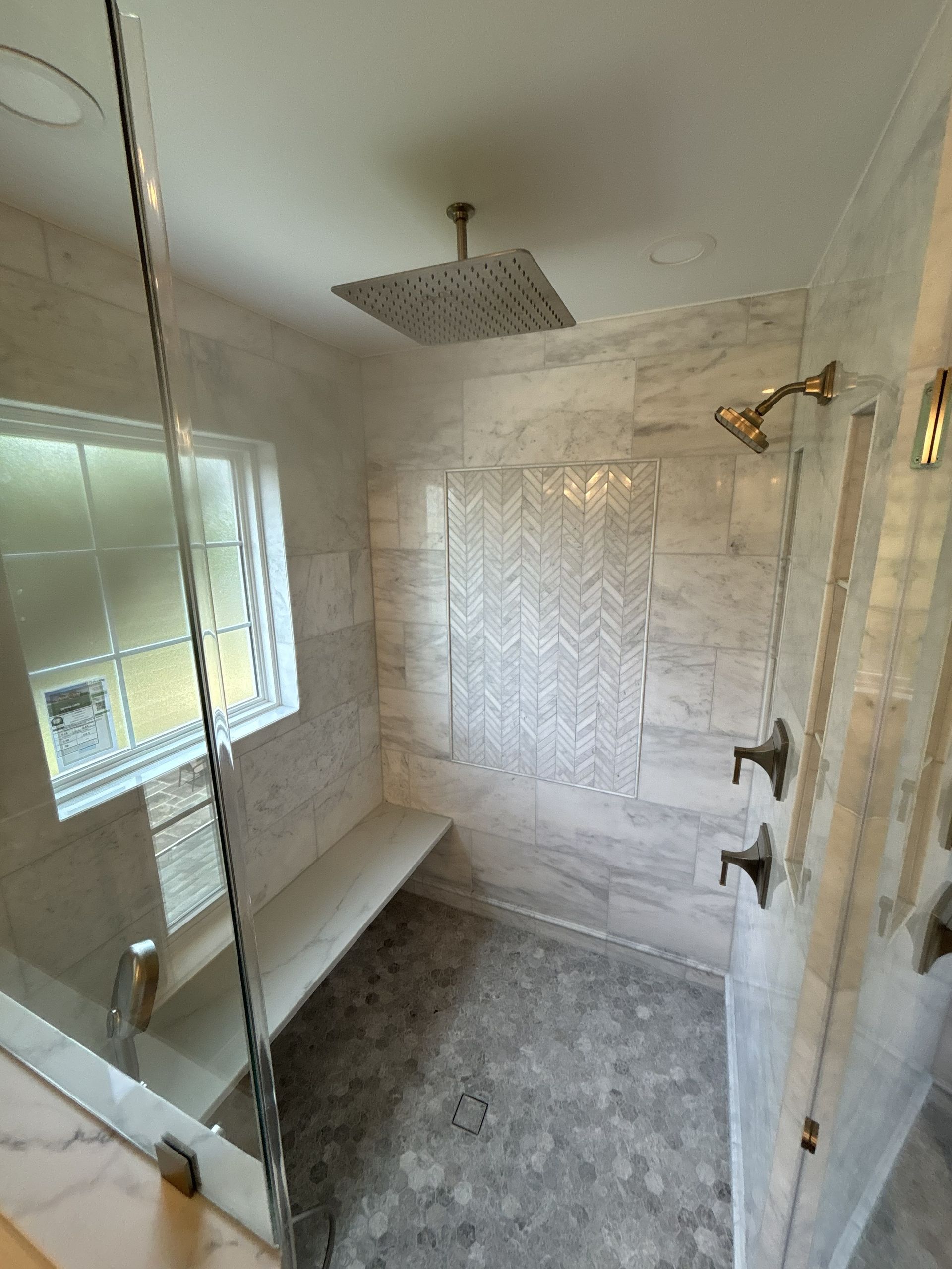 Small bathroom with glass shower, white tiled walls, and a built-in bench.