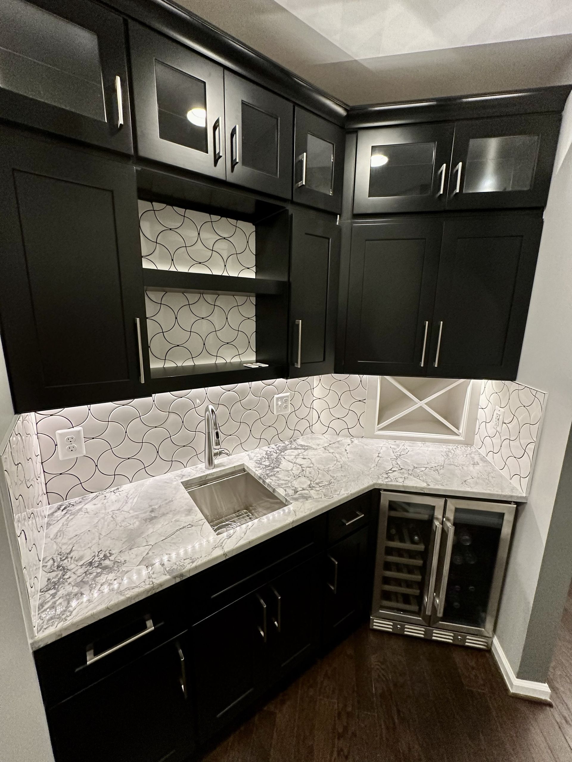 Dark kitchen corner with black cabinets, white tile backsplash, sink, and built-in wine fridge