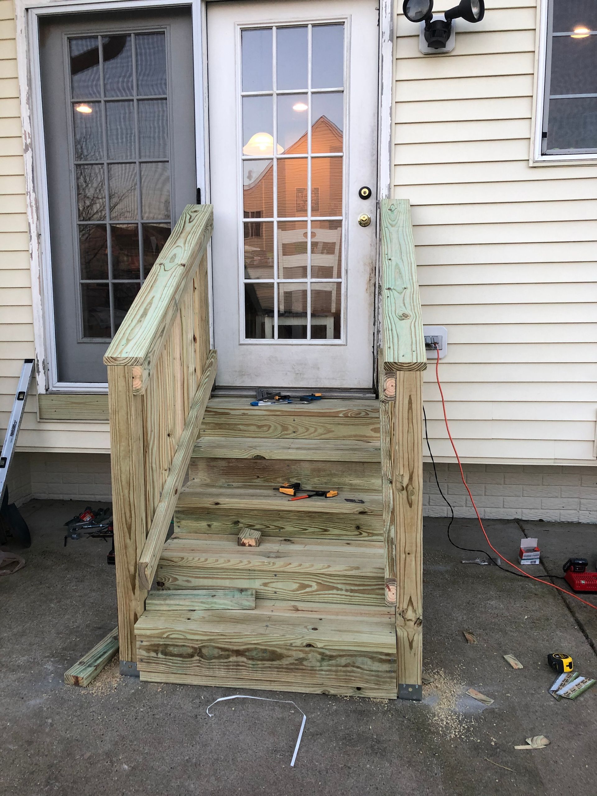 Weathered wooden wheelchair ramp leading to a back door beside a house siding and window.
