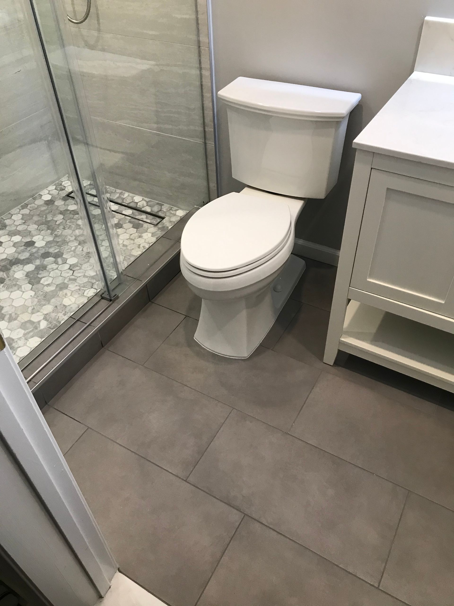 Small bathroom with white toilet, glass shower, and gray tile floor.