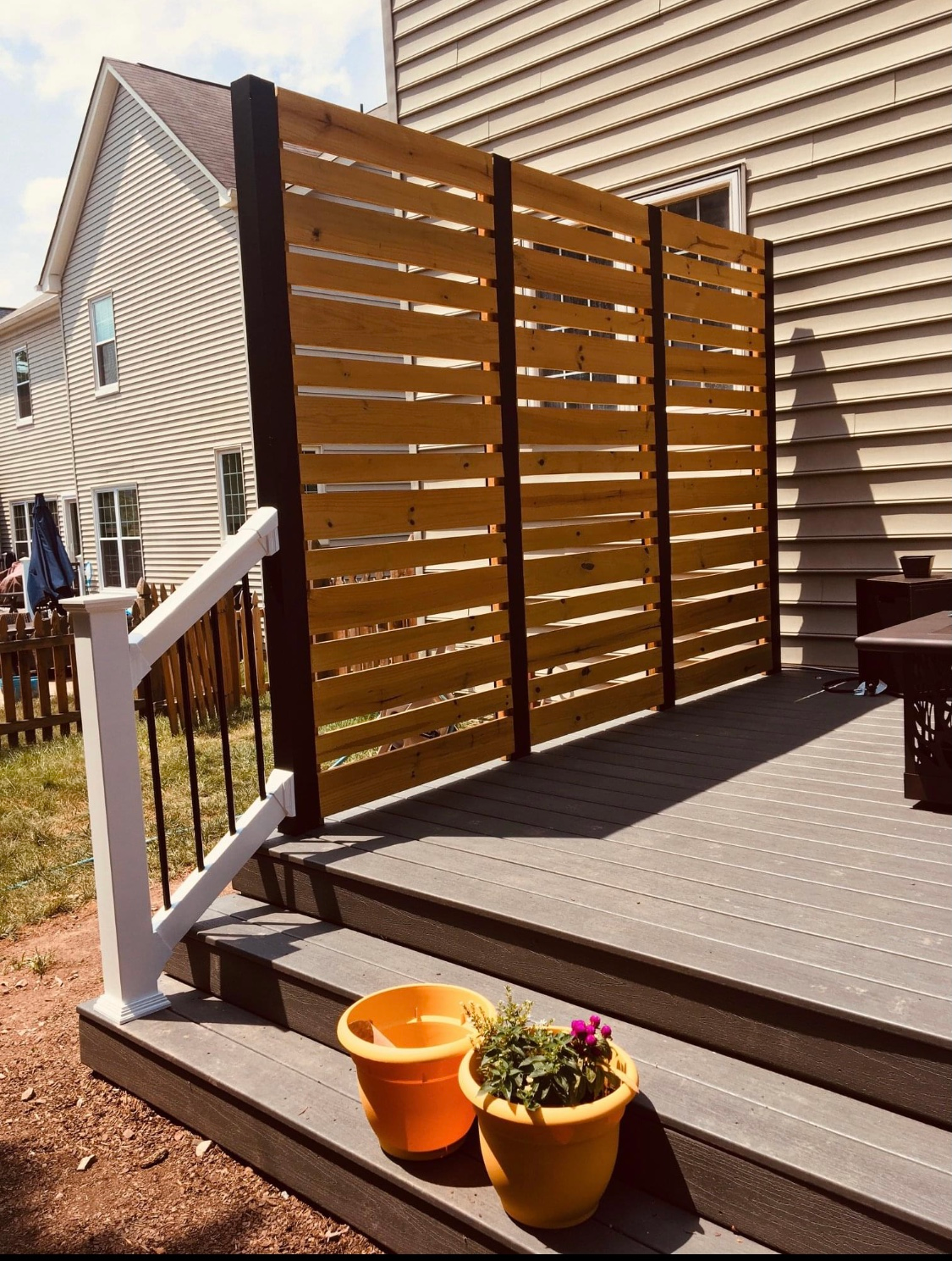 Backyard deck with white railing, wooden privacy screen, and two potted plants on the steps