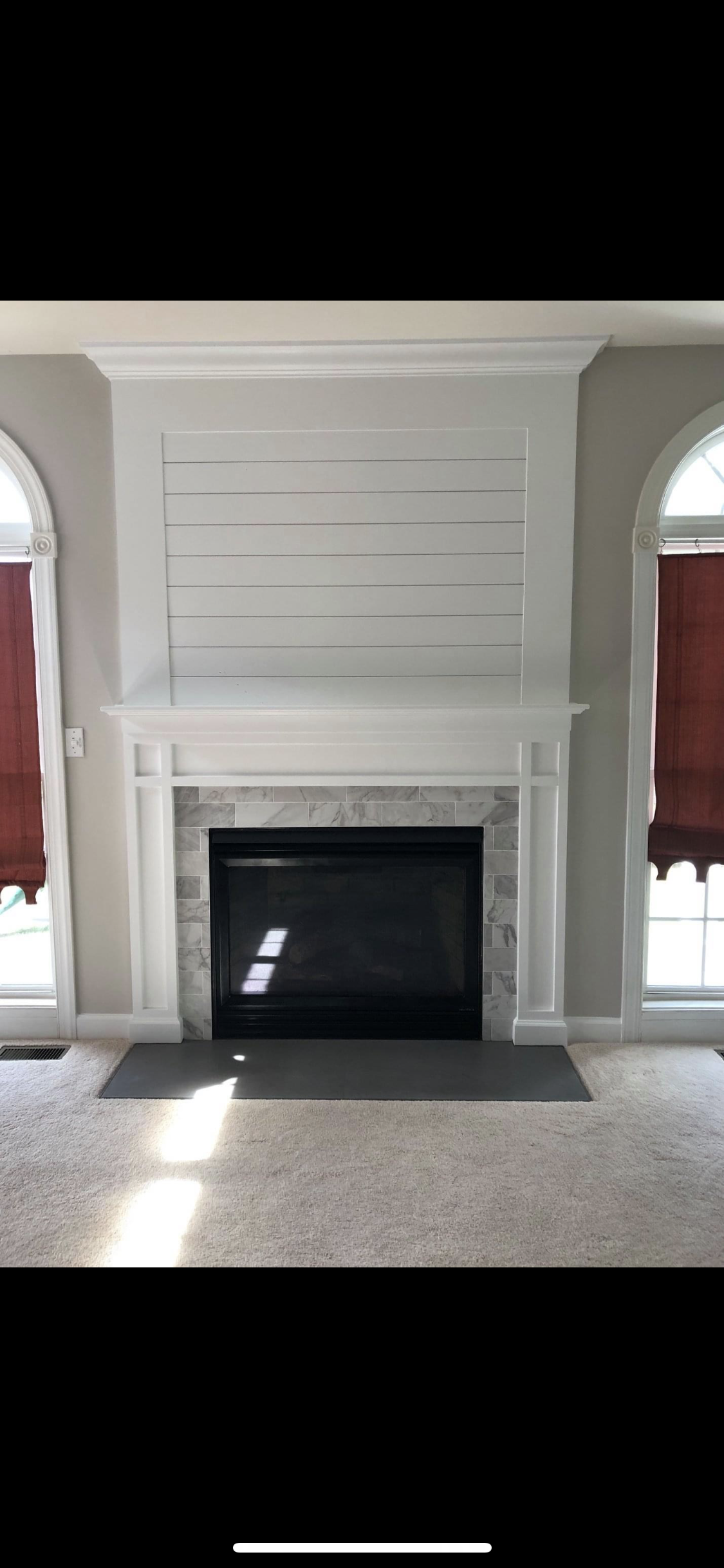 White fireplace in a bright room with arched windows and red curtains on both sides