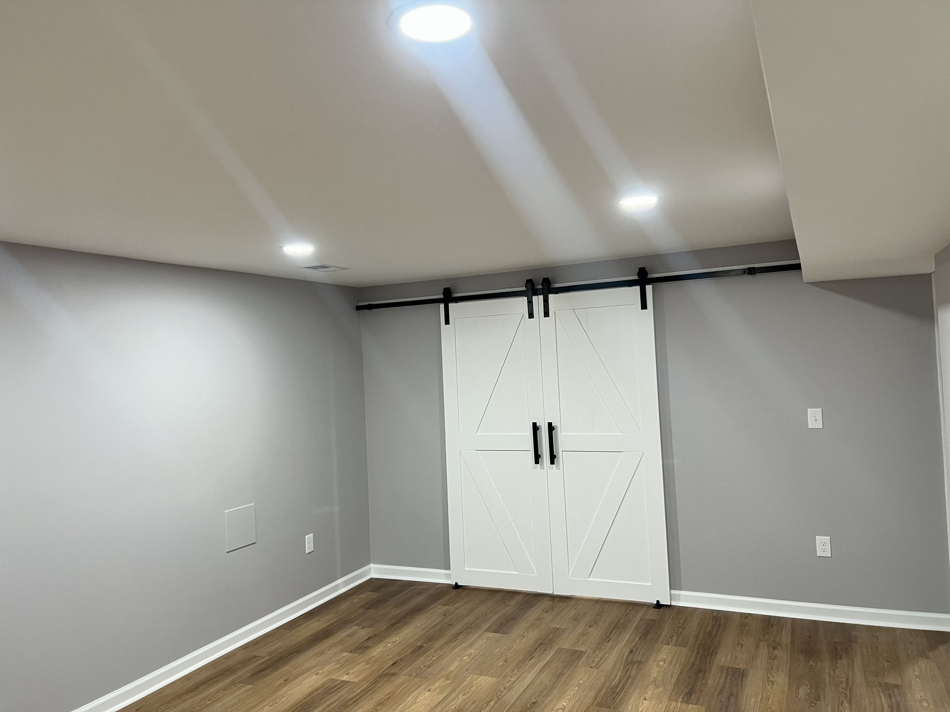 Empty gray room with wood floor, white double closet doors, and recessed ceiling lights