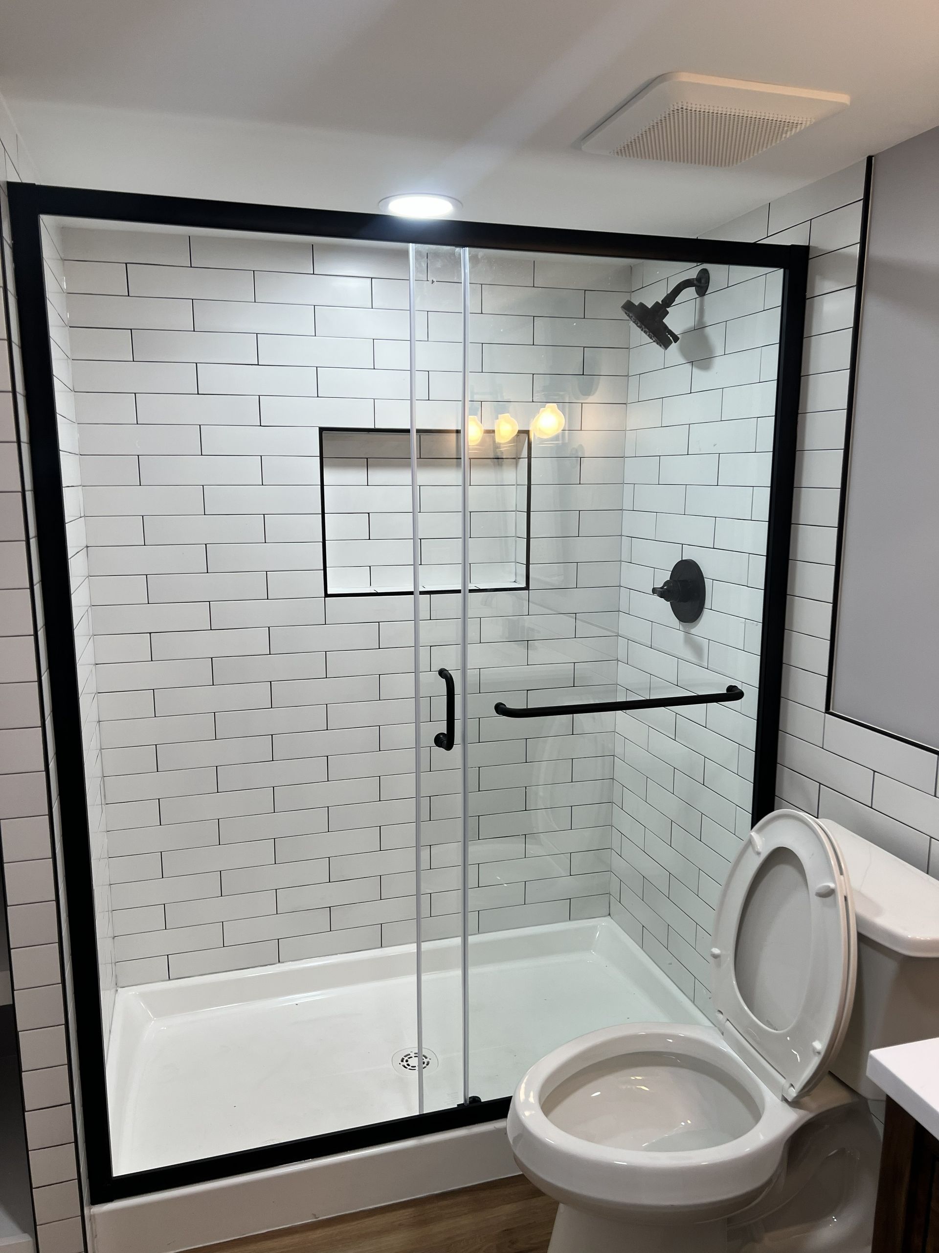 Modern bathroom with glass shower, white tiled walls, and an open toilet seat.
