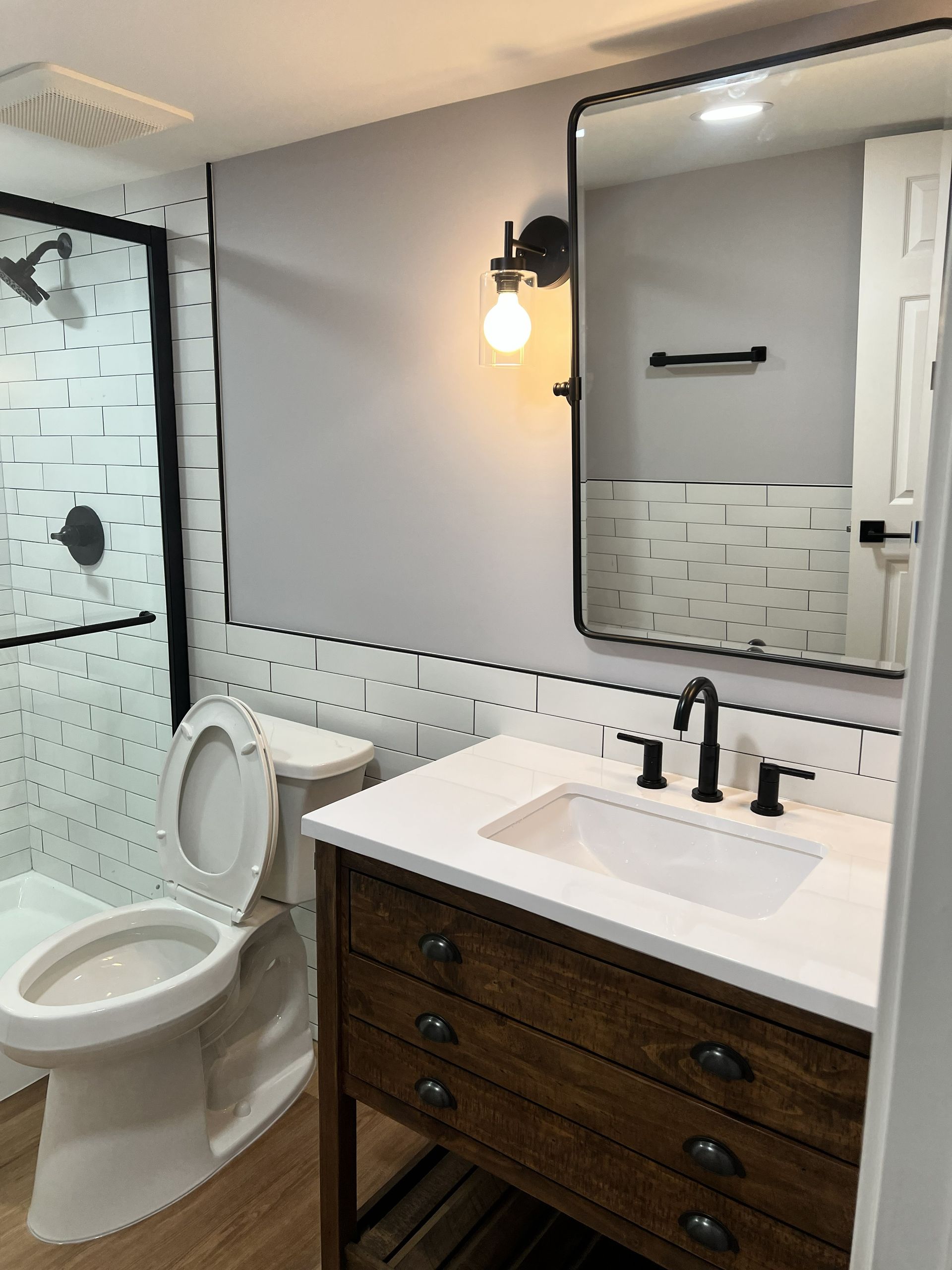 Modern bathroom with white toilet, wood vanity, large mirror, and glass shower enclosure