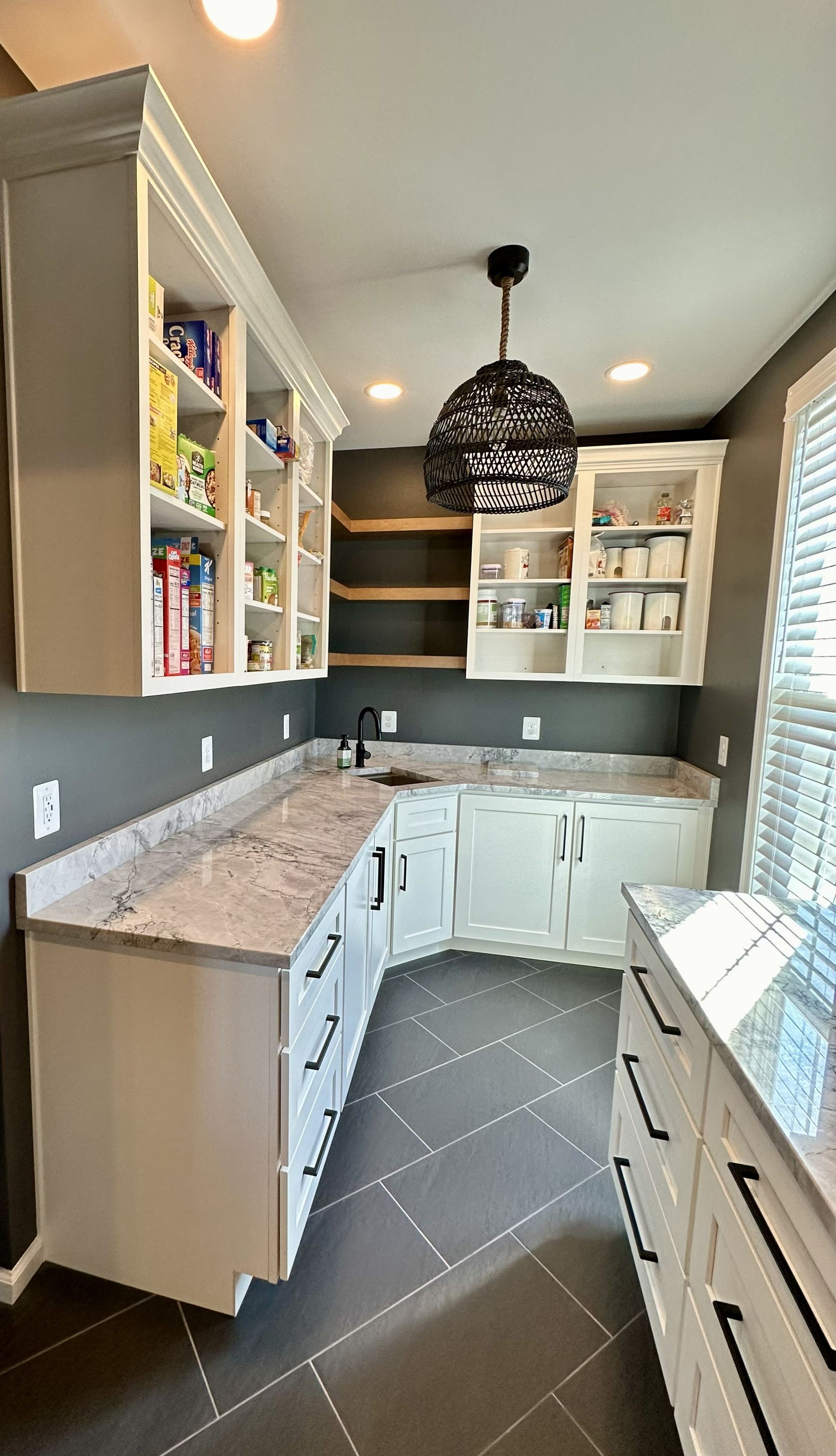 Bright kitchen with white cabinets, marble countertops, dark tile floor, and black pendant light.