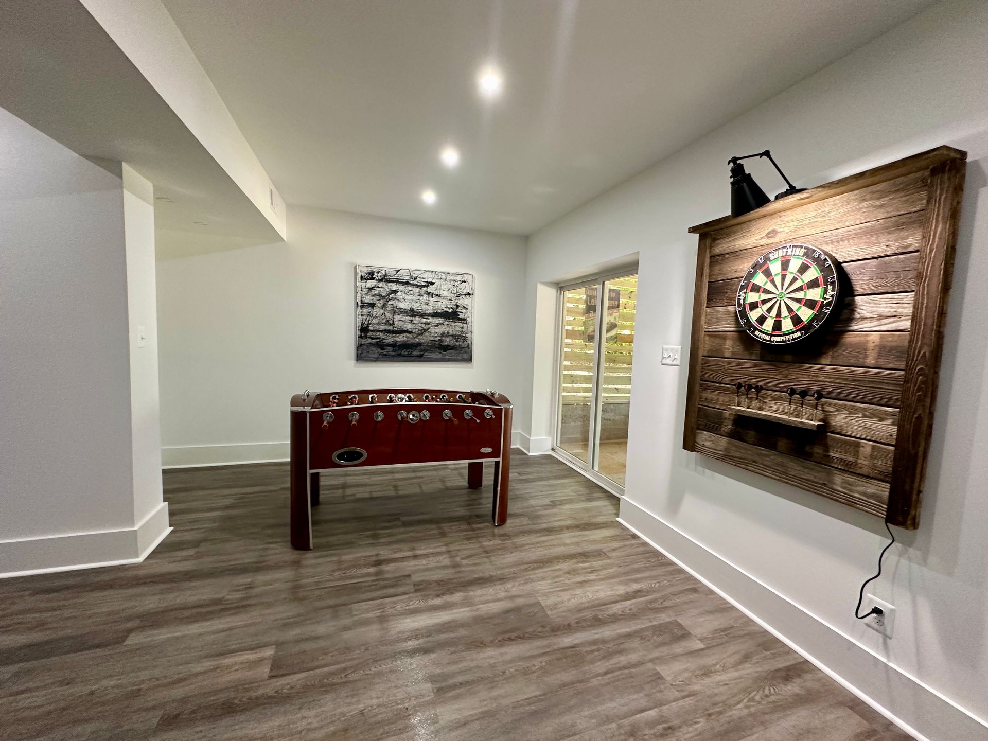 Basement rec room with a red foosball table and wall-mounted dartboard on a wood accent wall.