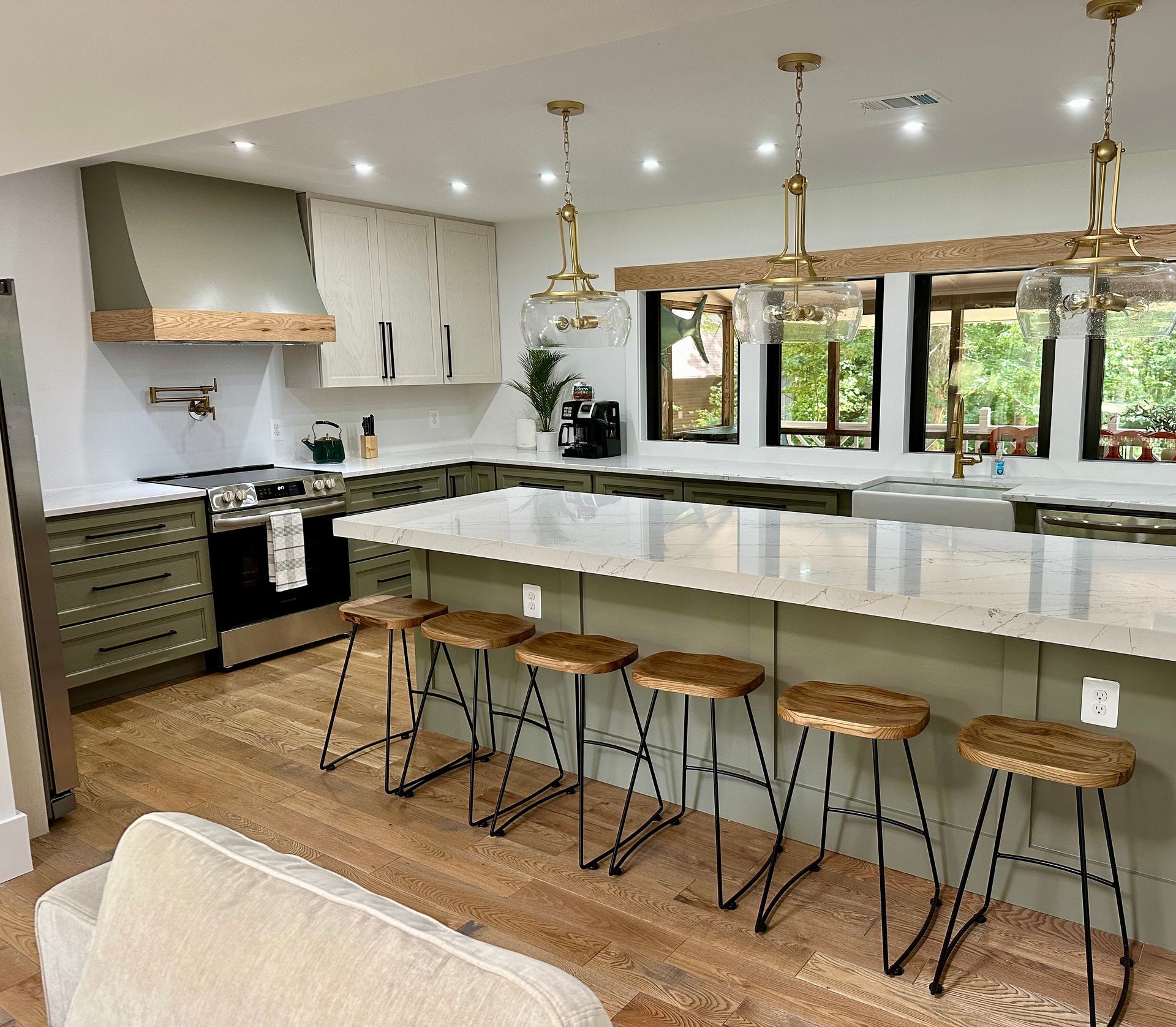 Modern kitchen with marble island, wooden stools, white cabinets, and large windows overlooking greenery