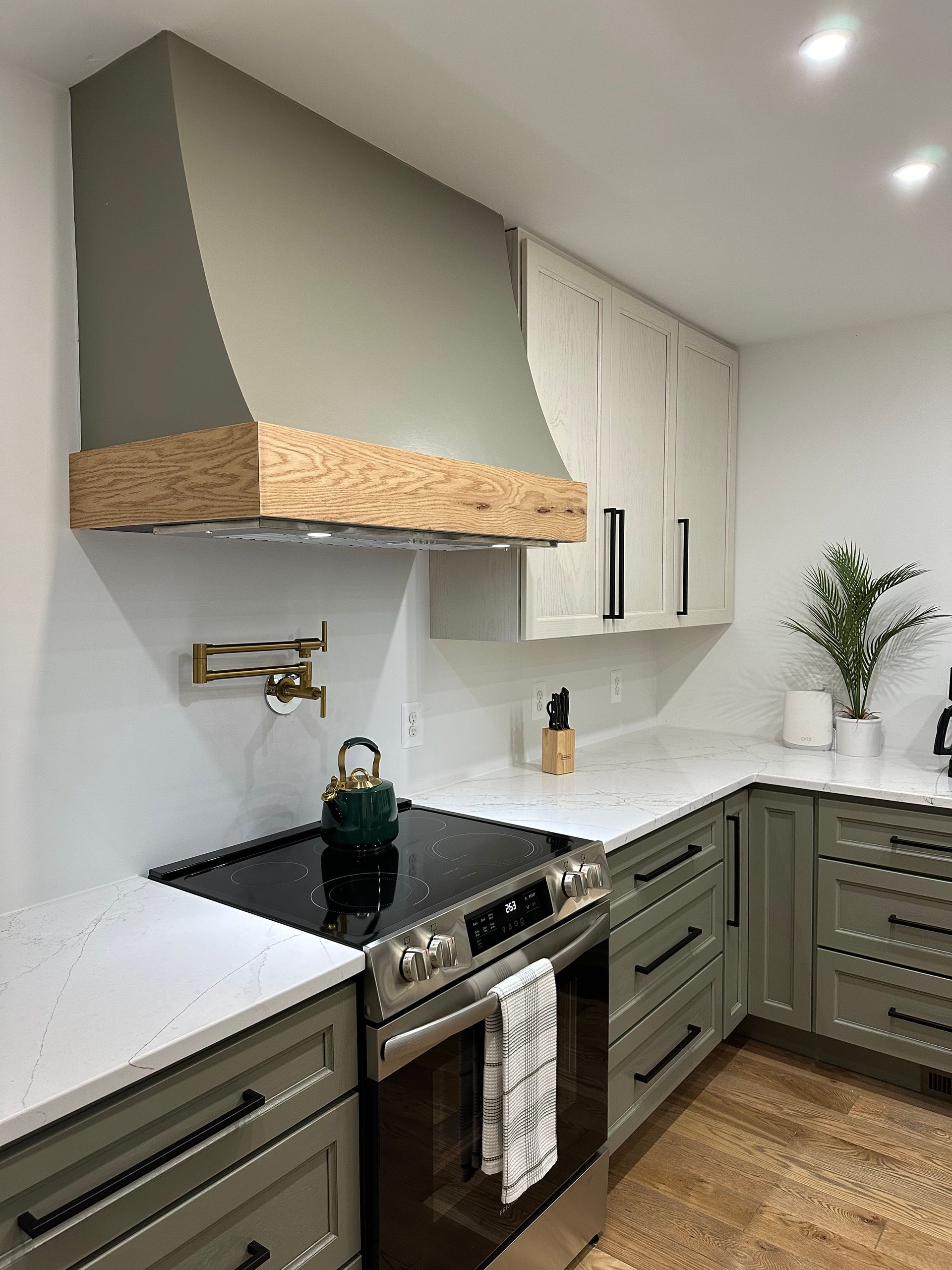 Modern white-and-olive kitchen with wood accents, black stove, and marble countertops.