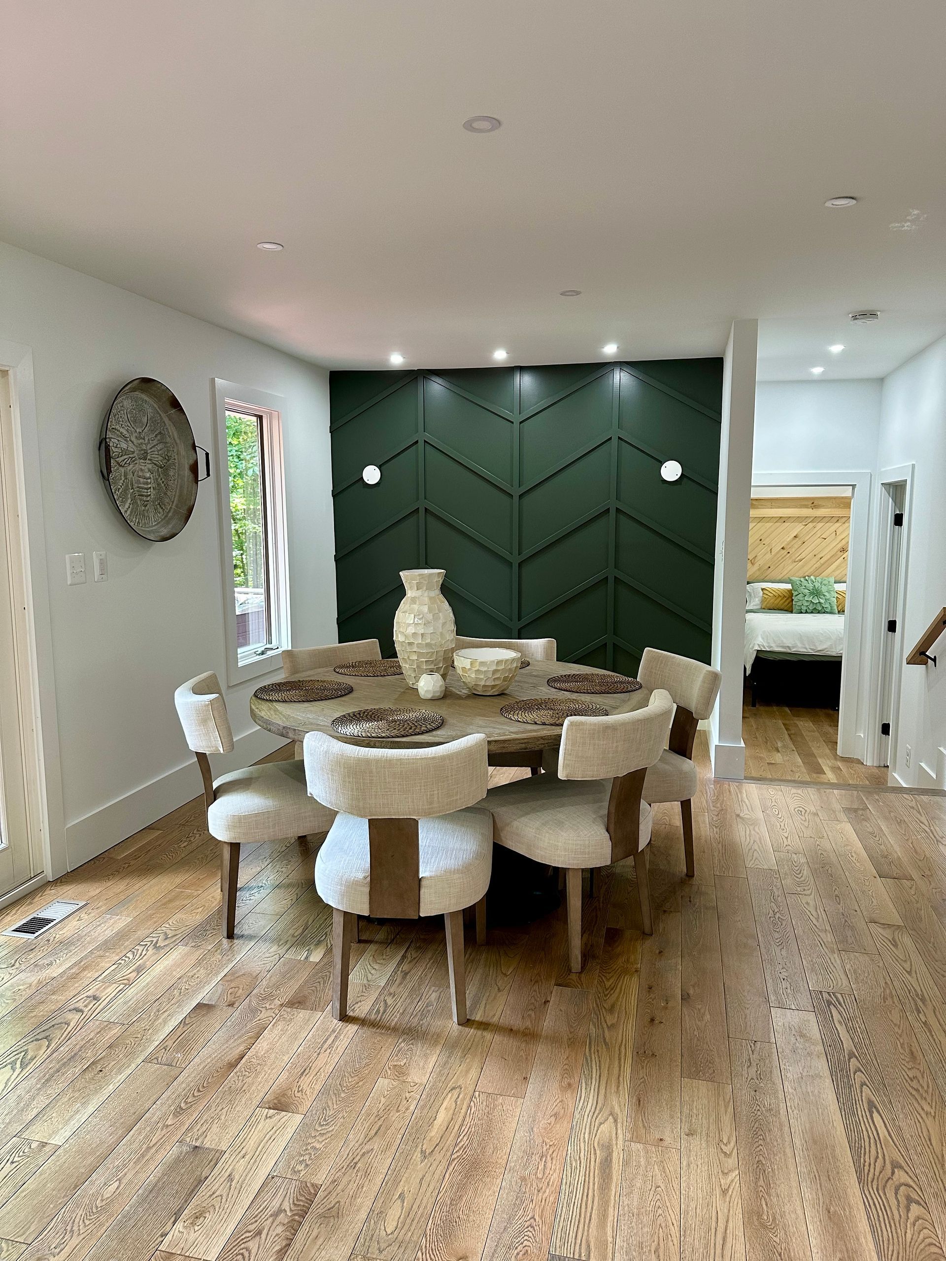 Modern dining room with green accent wall, round table, and upholstered chairs
