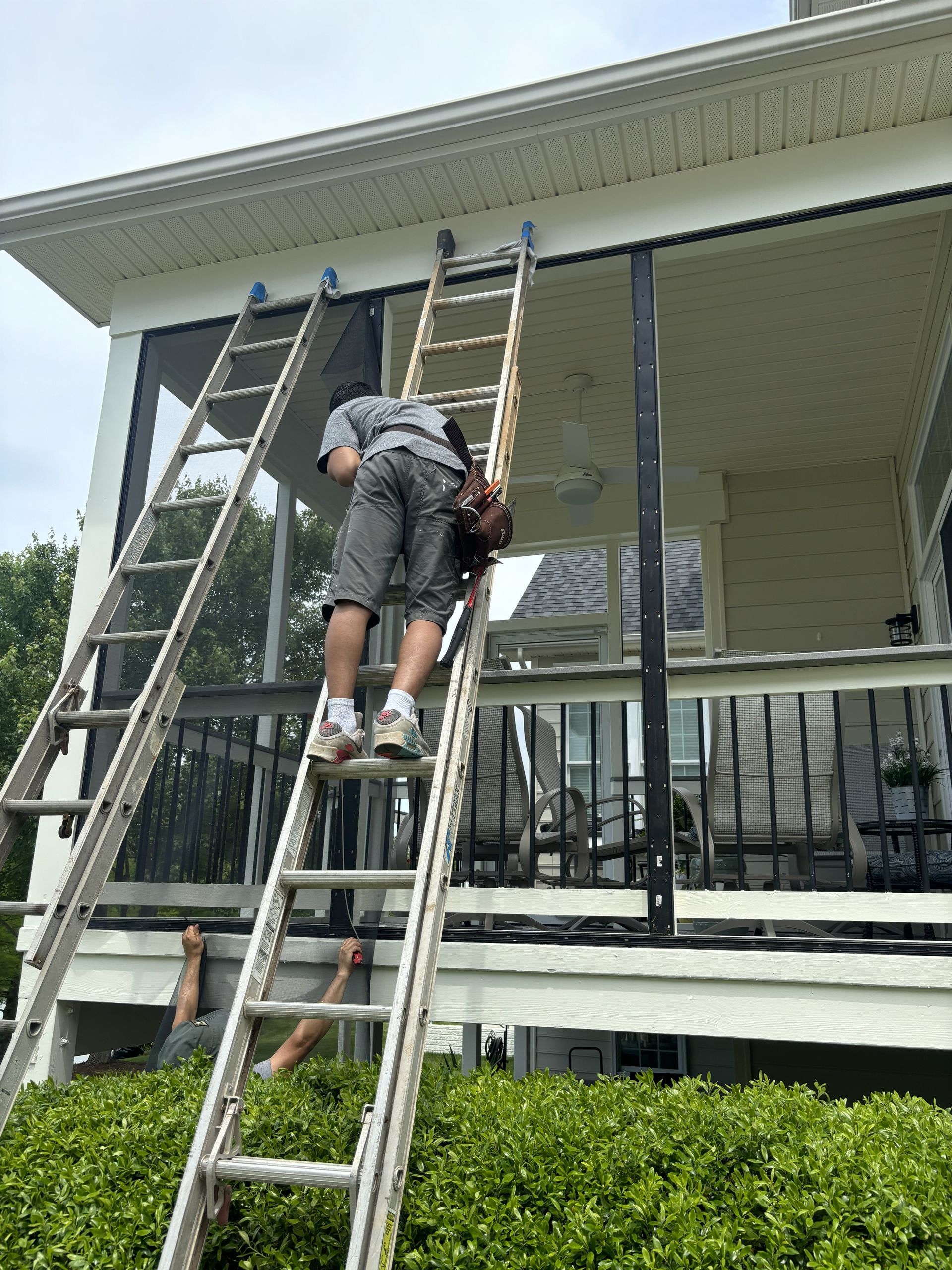 Person on a ladder working on a porch railing beside a house.