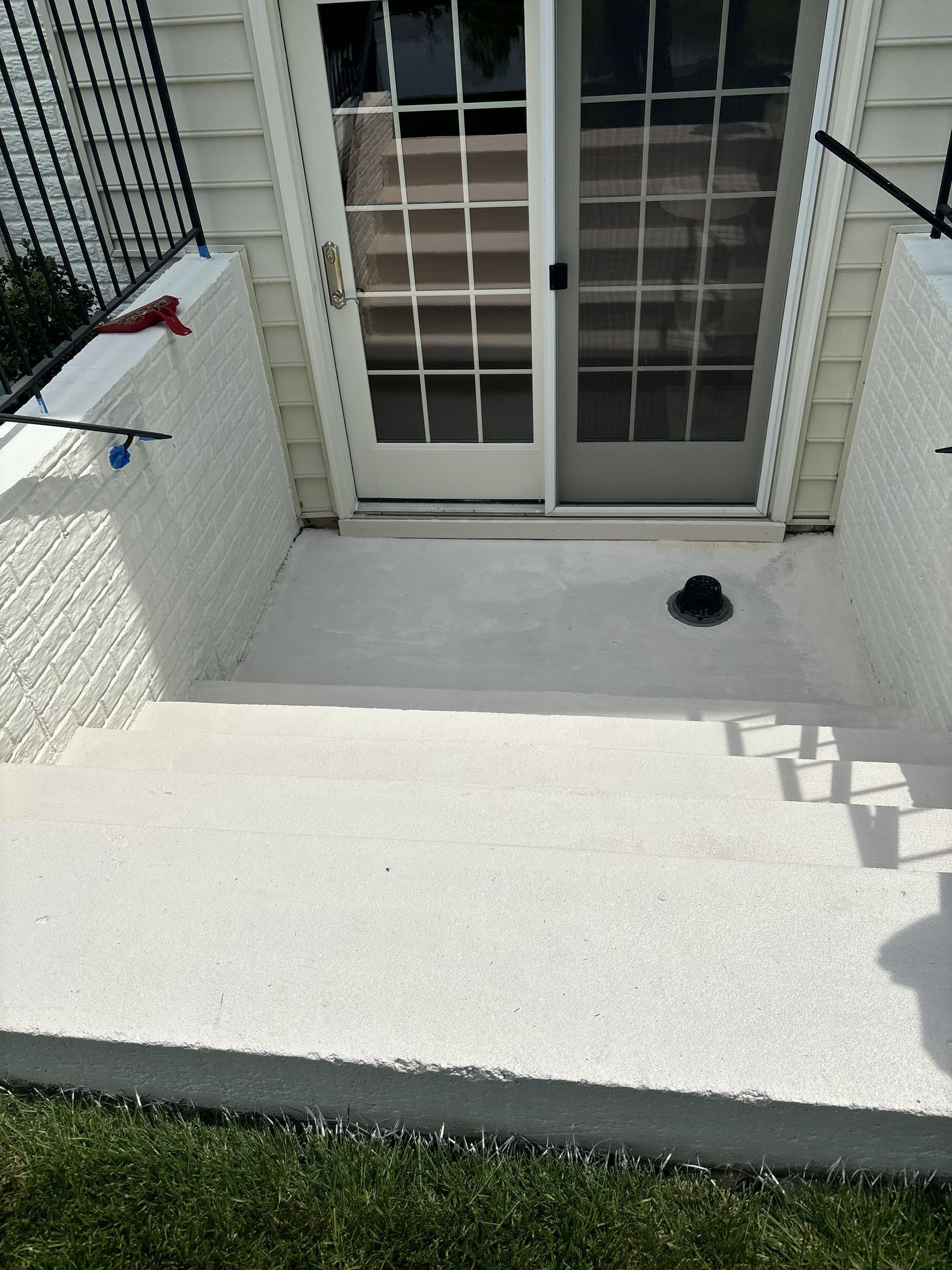 Concrete patio in front of white sliding glass doors, with a small black item near the threshold.