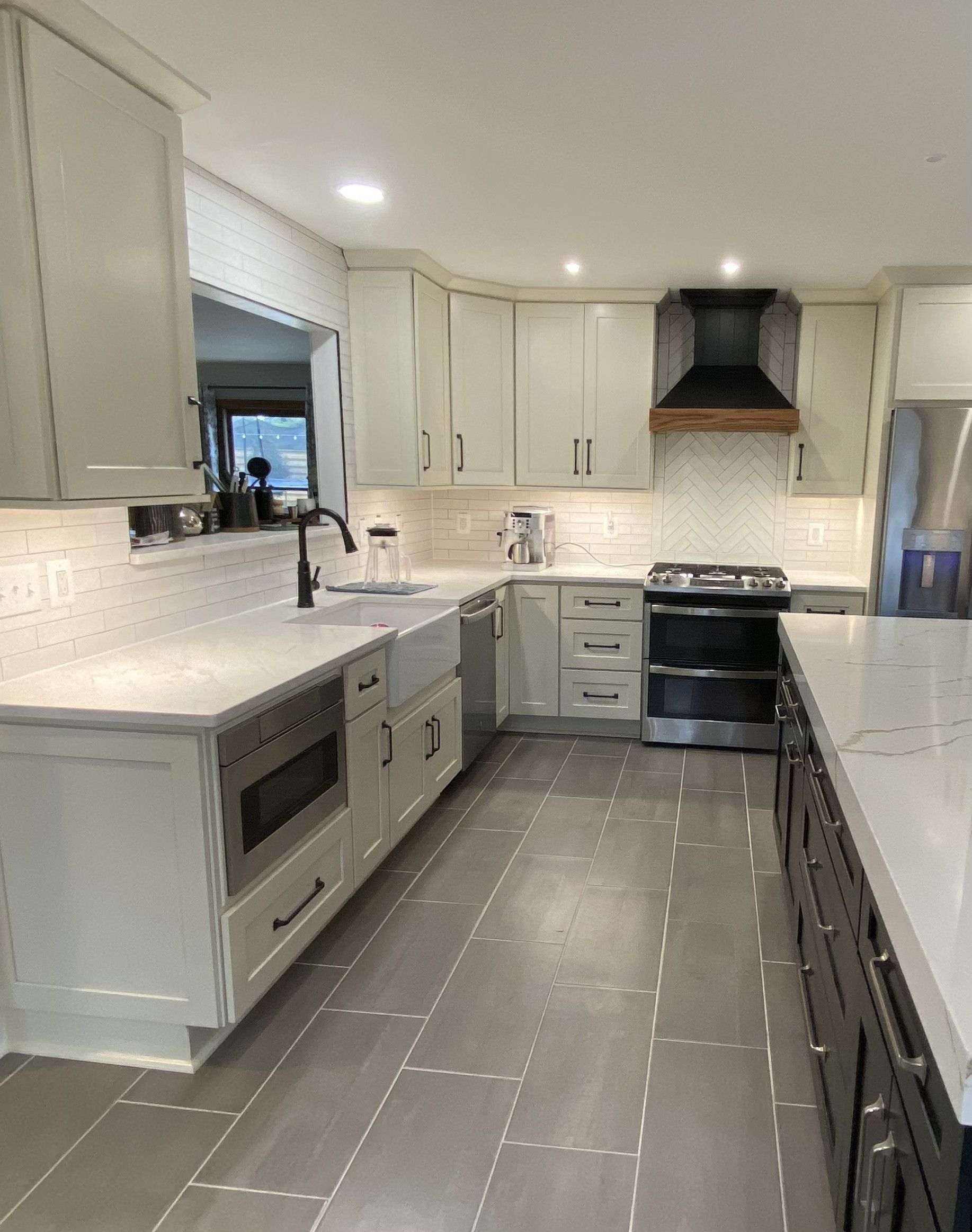 Bright modern kitchen with white cabinets, dark stove, marble counters, and gray floor runner