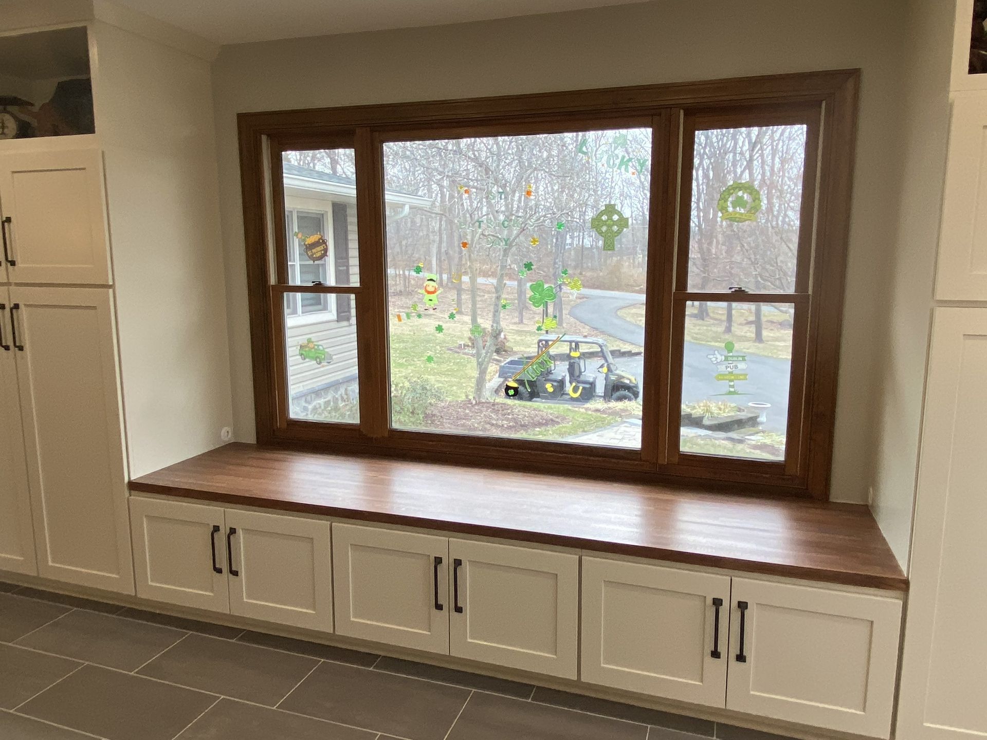 Built-in window seat with white cabinets beneath a large wood-framed window overlooking a yard