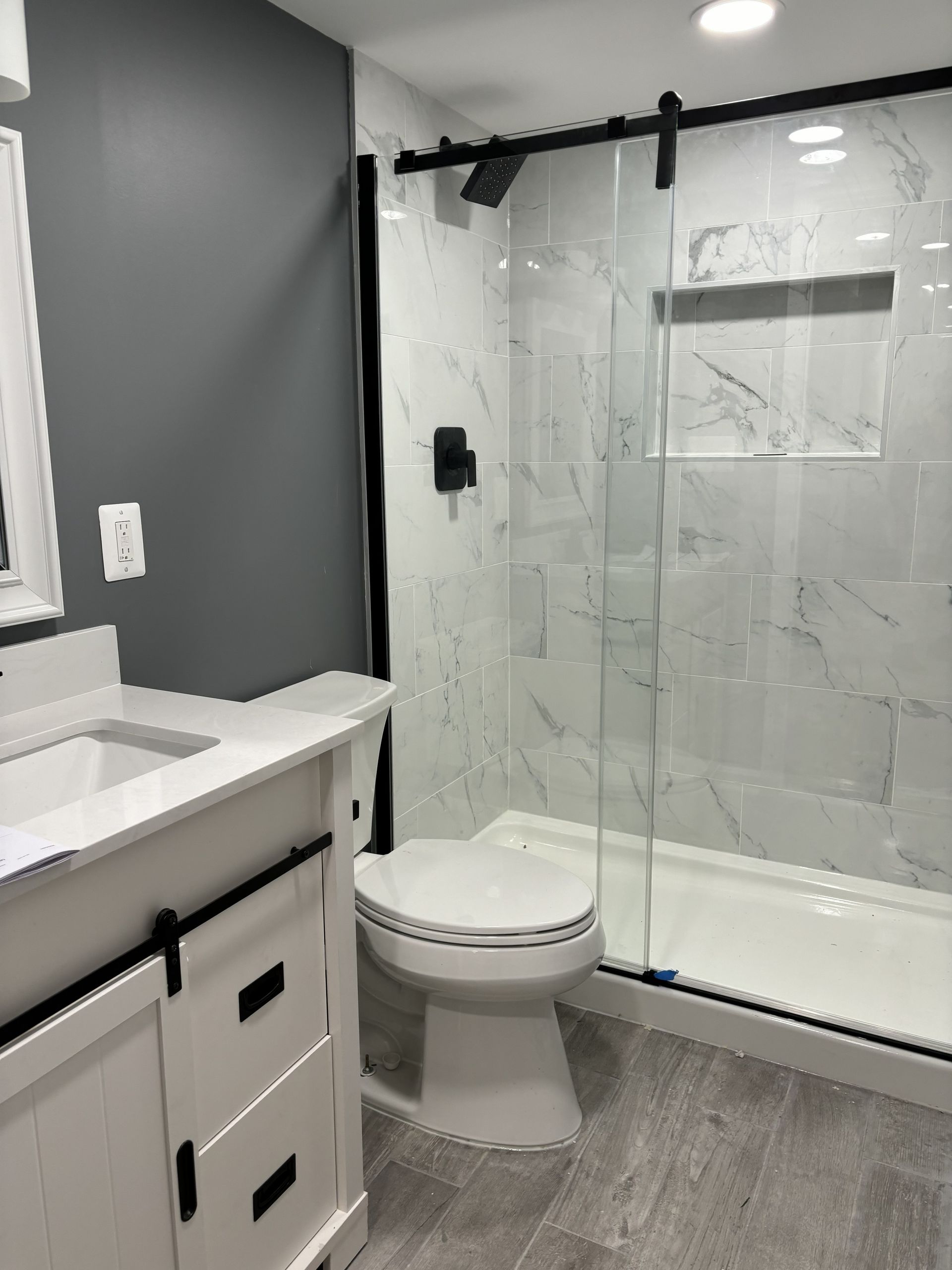 Modern bathroom with white vanity, toilet, and glass shower enclosure with marble tile.