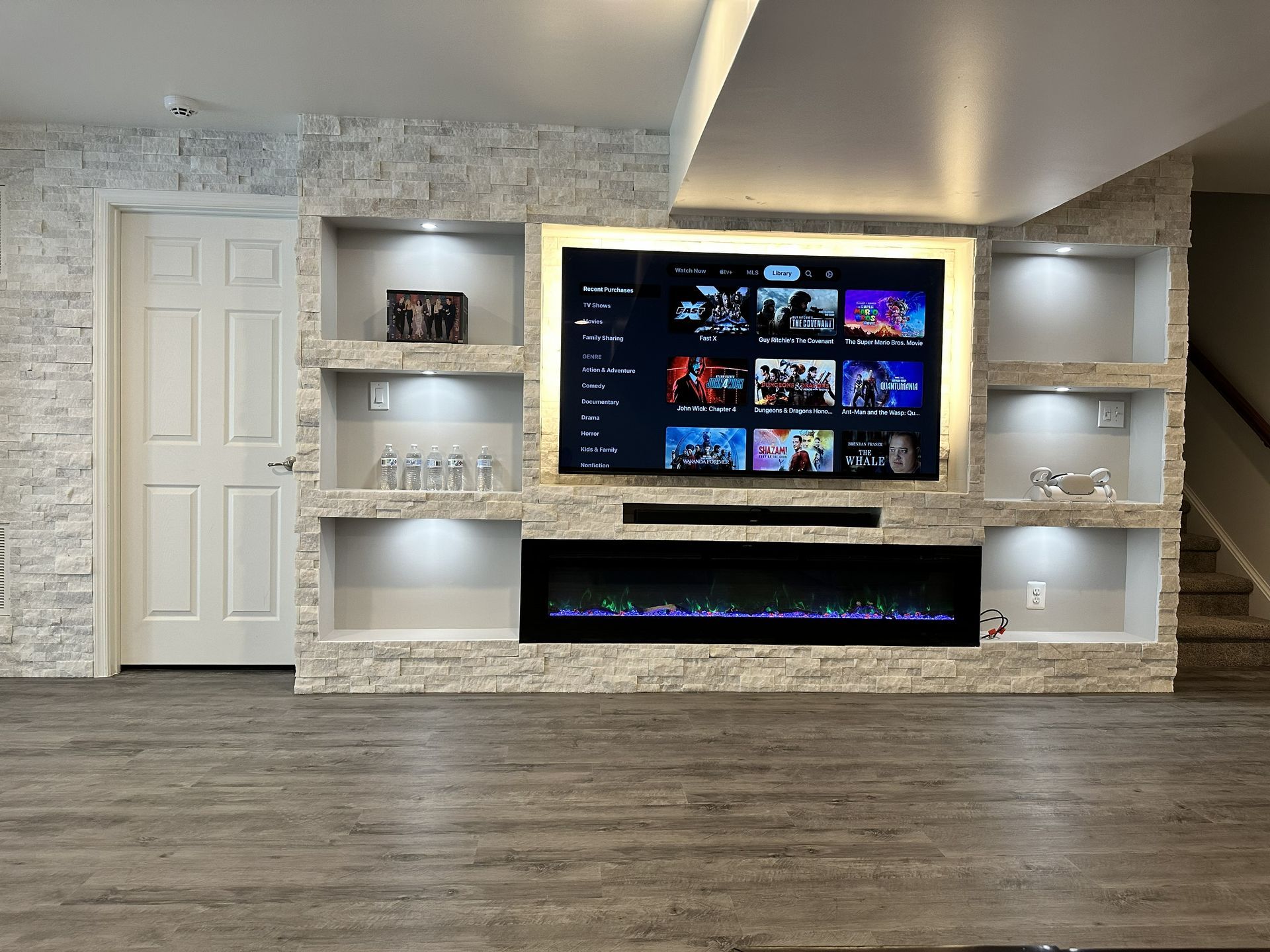 Modern living room with built-in TV wall, fireplace, recessed shelves, and gray wood flooring