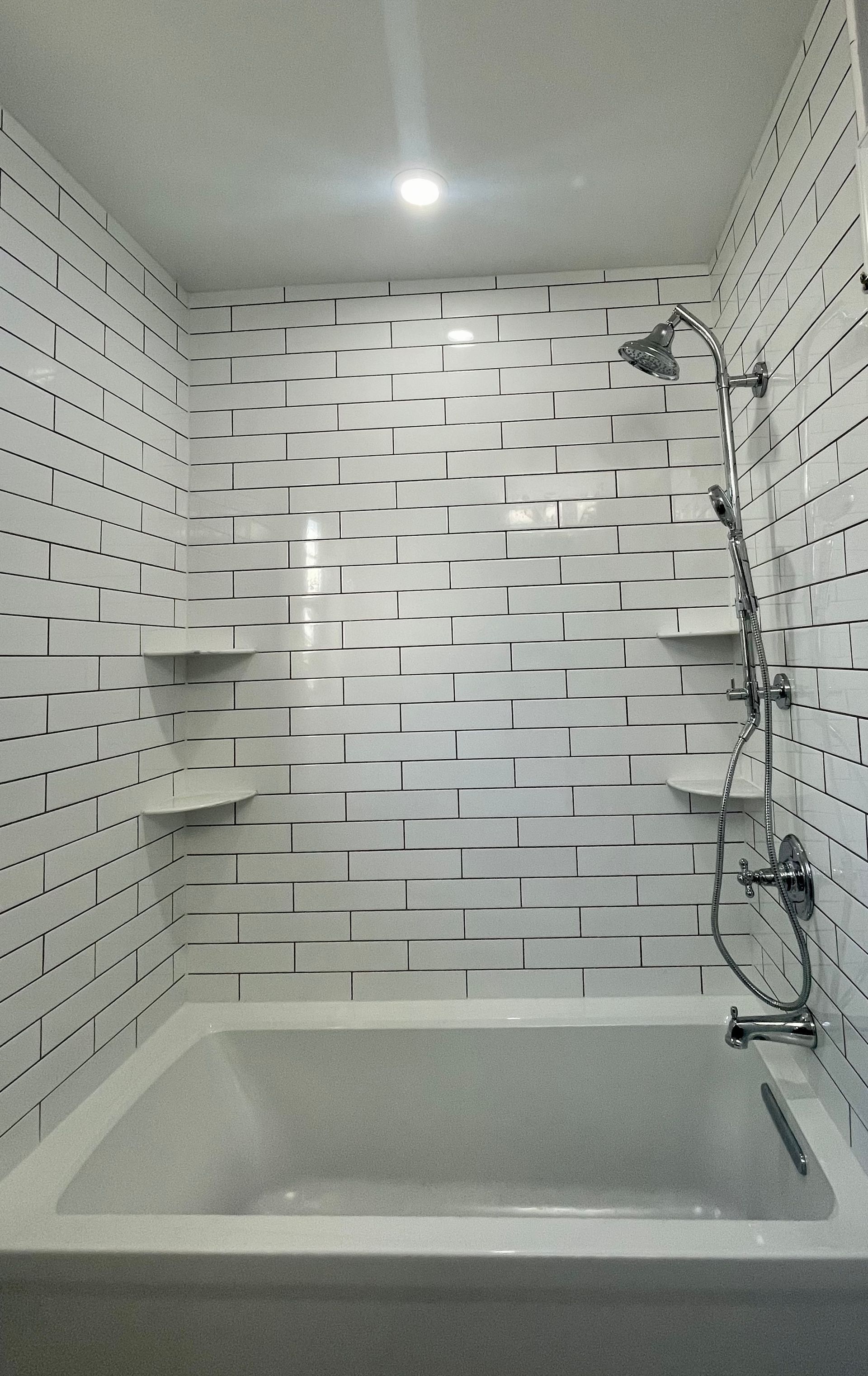Small white-tiled bathroom with a bathtub, showerhead, and ceiling light