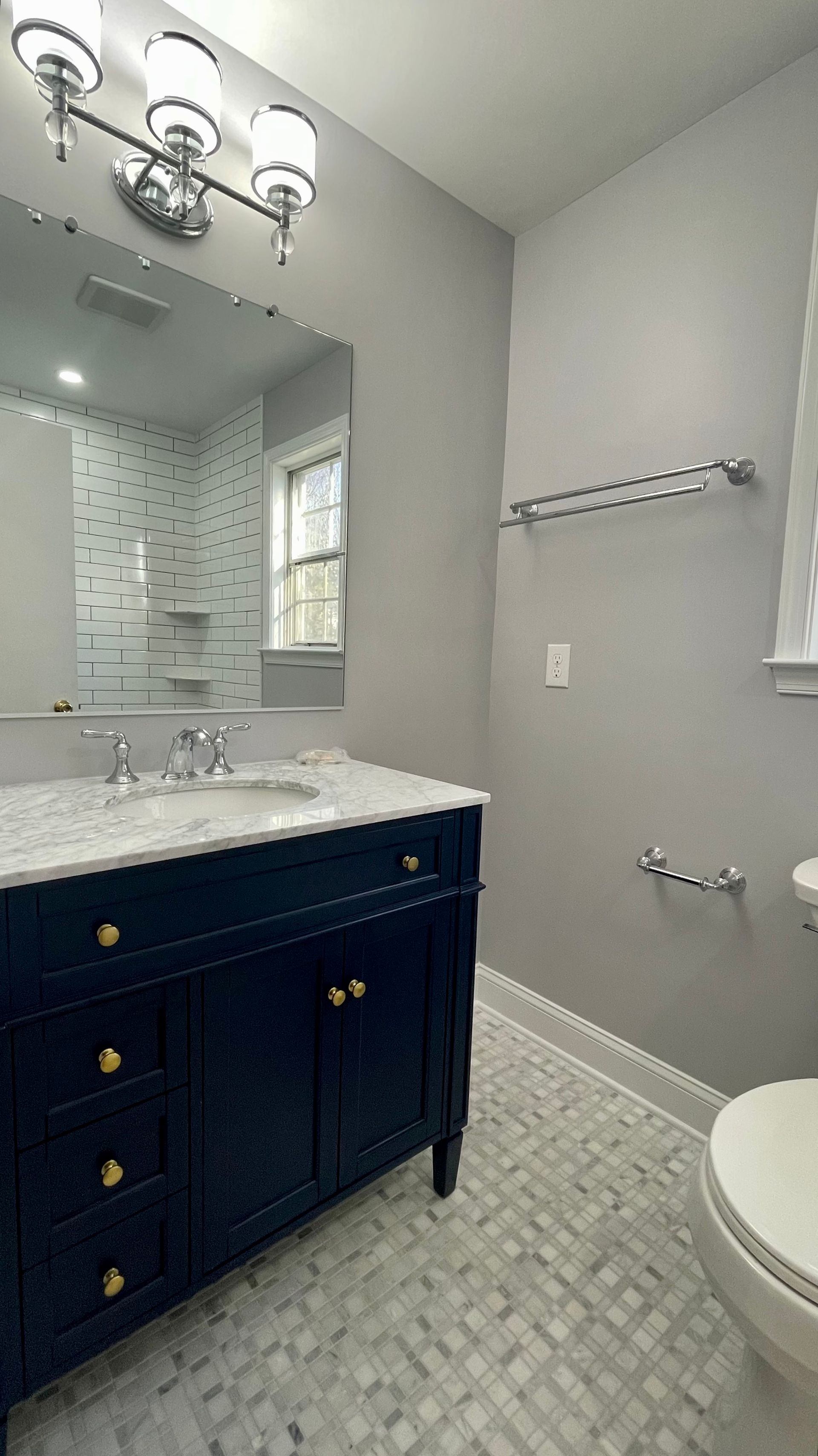 Small gray bathroom with navy vanity, white sink, mirror, and partial toilet visible