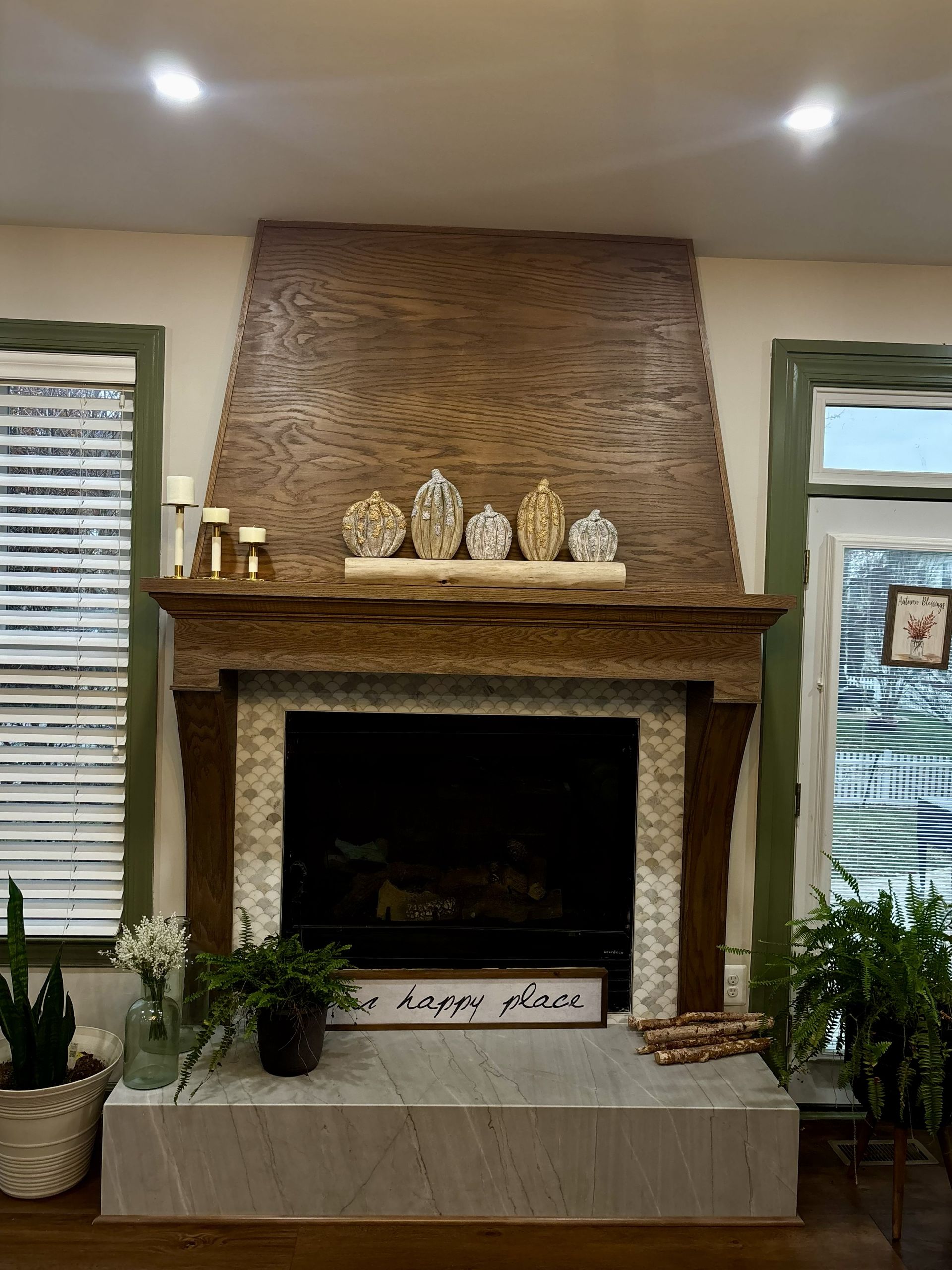 Living room fireplace with wood mantel, decorative figurines, plants, and woven wall paneling