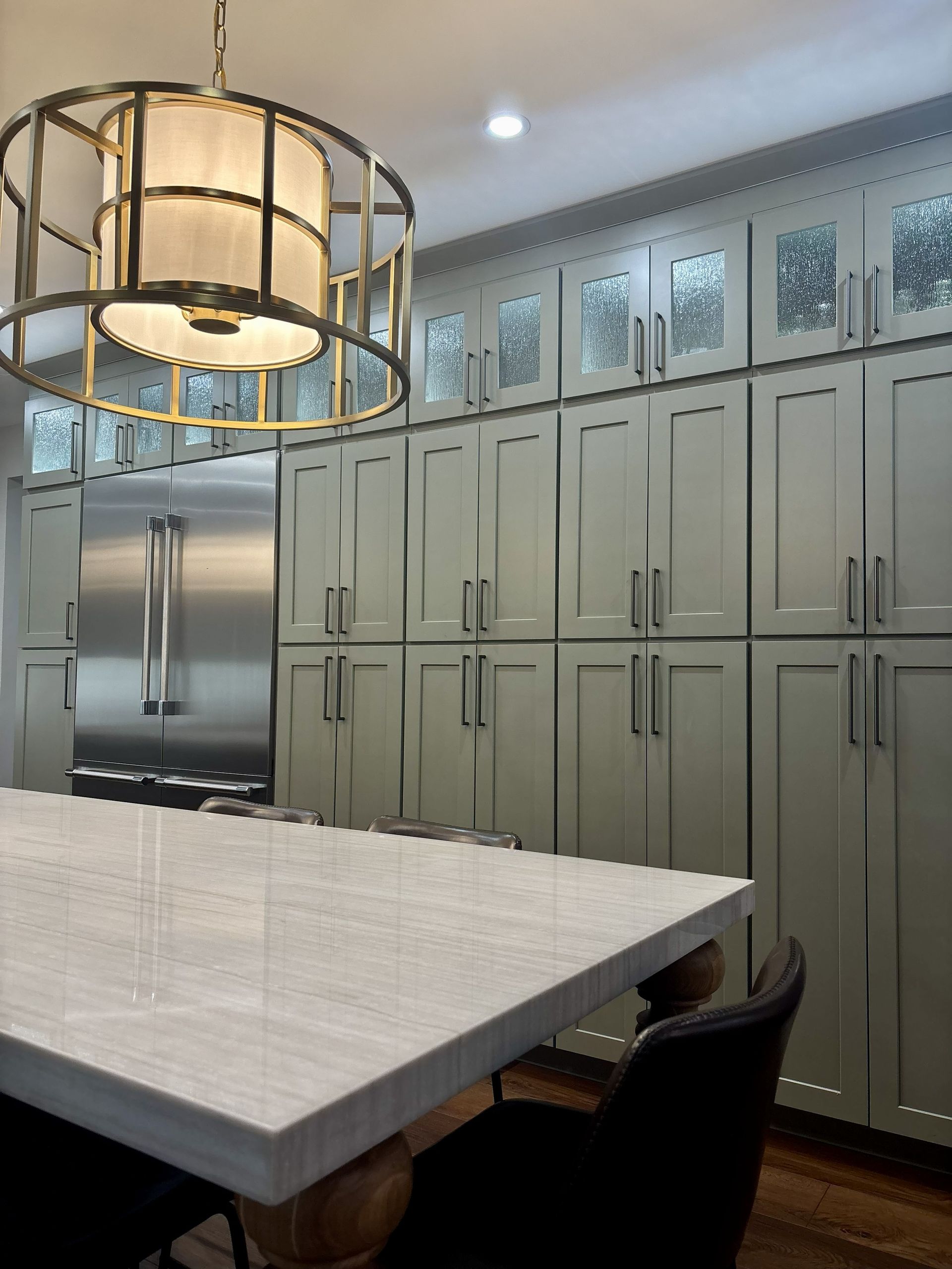 Modern kitchen with white island, stainless fridge, tall cabinets, and a large round pendant light