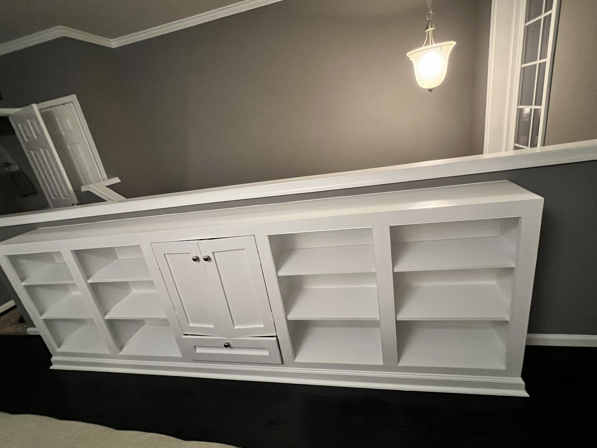 White built-in cabinet shelving along a wall in a gray room, with a light fixture above.