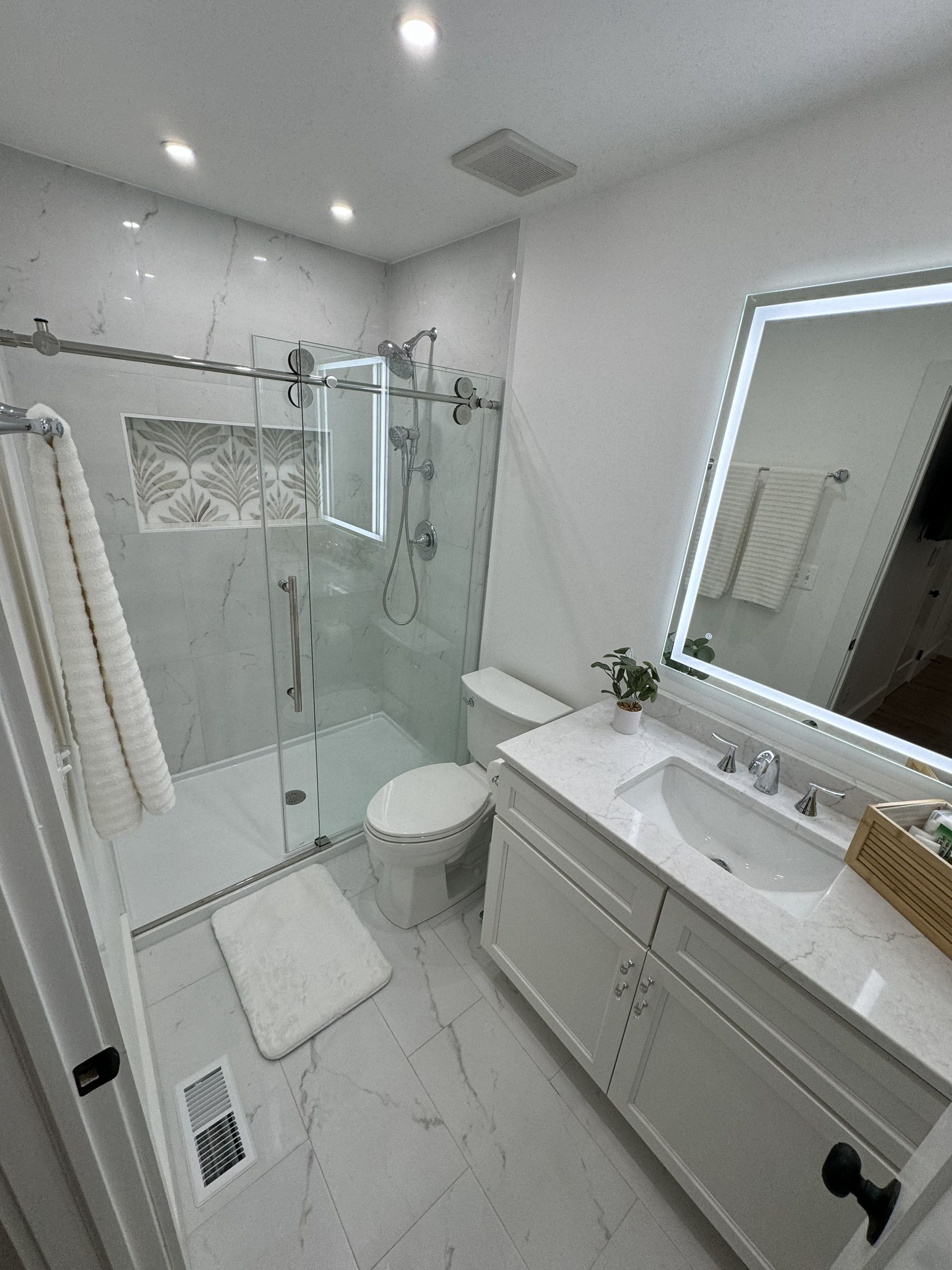 Modern white bathroom with shower, toilet, vanity, and illuminated mirror