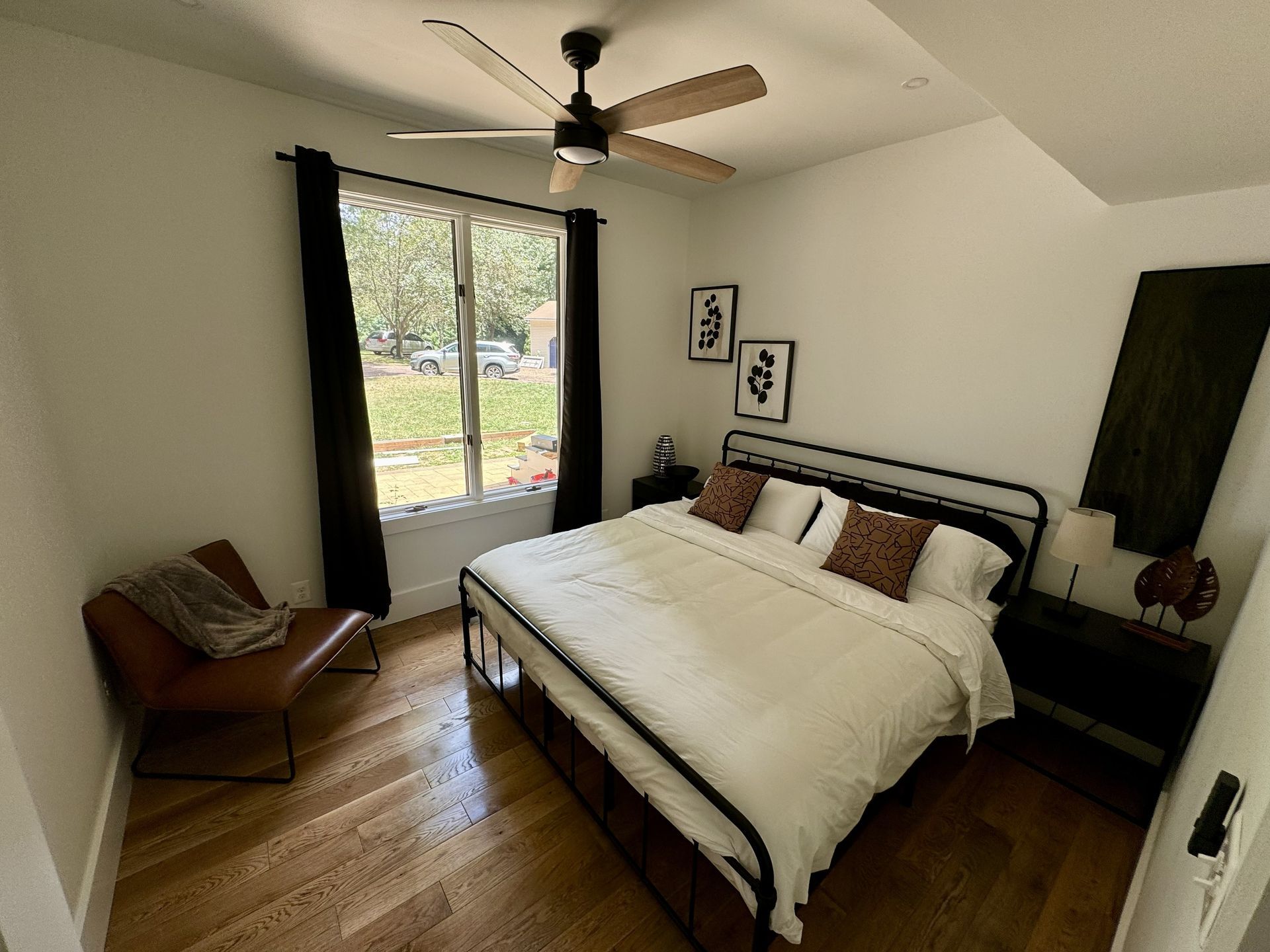 Modern bedroom with black bed frame, large window, wood floor, and ceiling fan